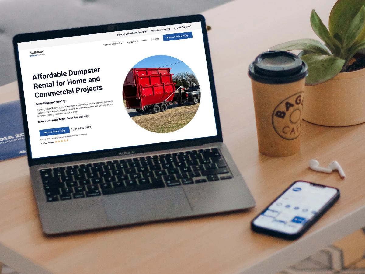 Laptop on a cafe table showing the Wise Guys Dumpsters Affordable Dumpster Rental for Home and Commercial Projects hero with a red roll off dumpster on a trailer