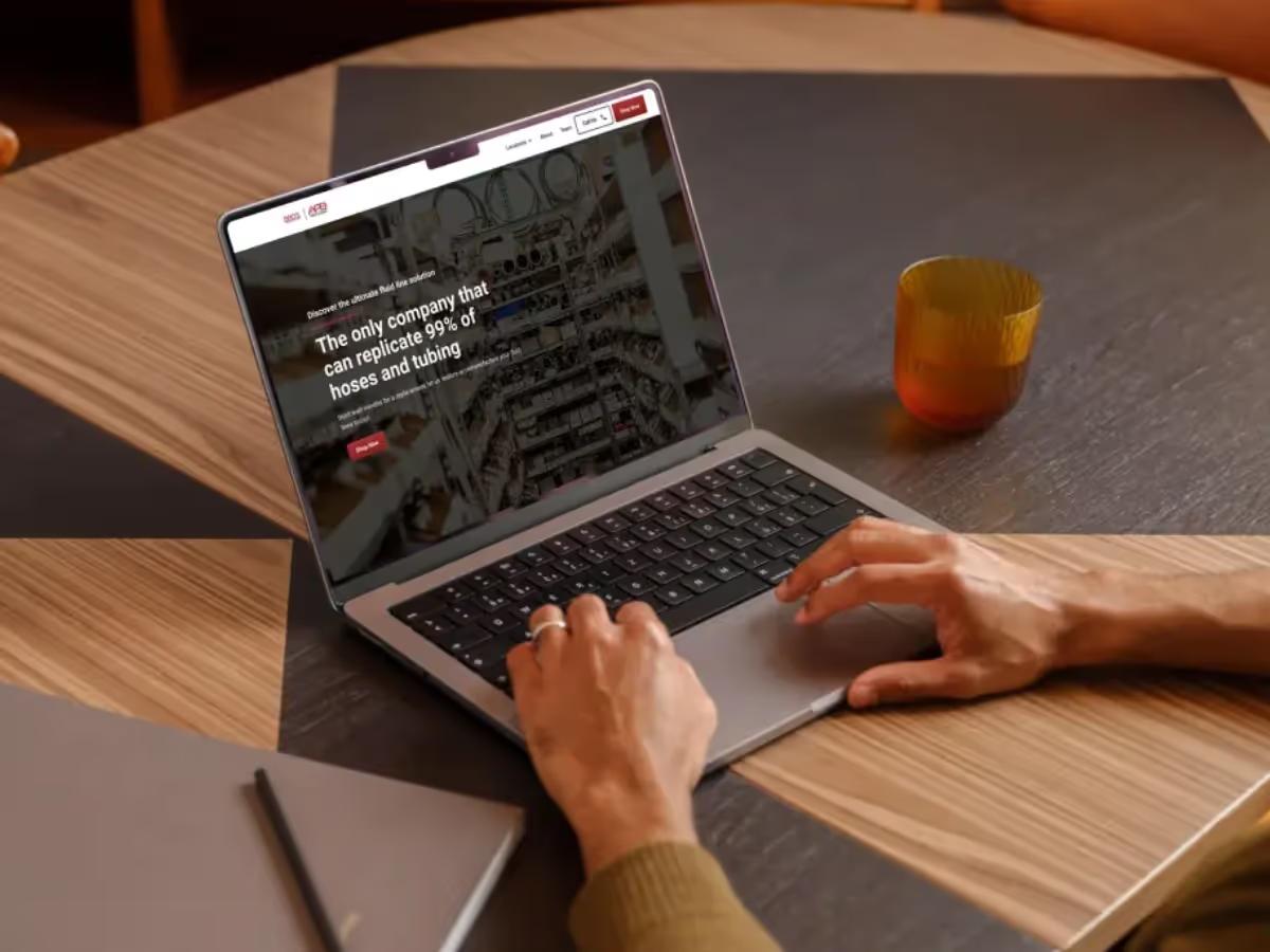 Laptop on a wooden table showing the Fluid Line Solutions homepage hero, The only company that can replicate 99% of hoses and tubing