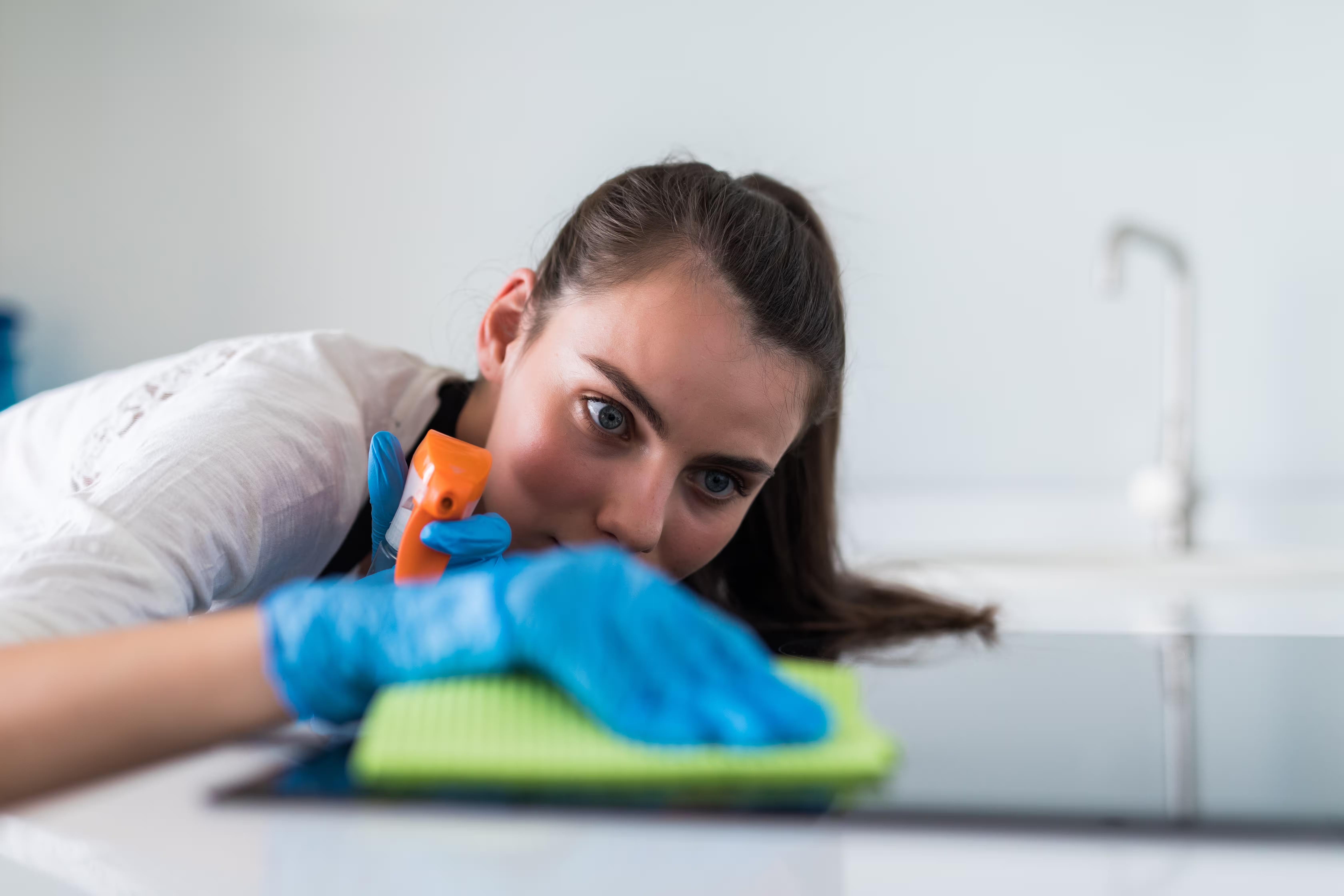 A cleaner checking her work up close while wiping down a cooktop, the finished detail worth photographing as proof before leaving the job.