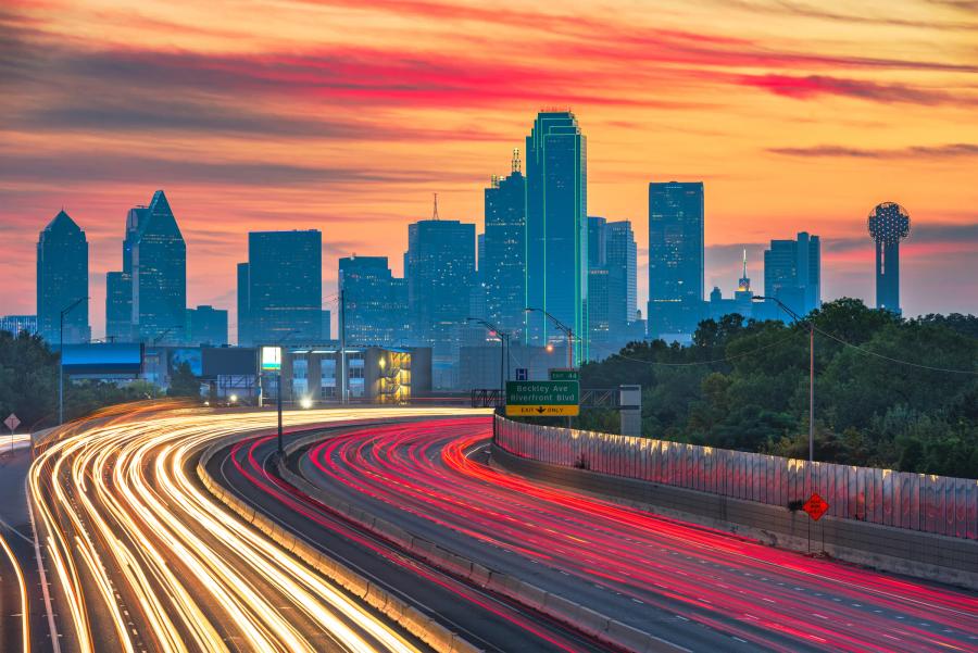 Vehicle light trails on a Dallas highway with the skyline at sunset