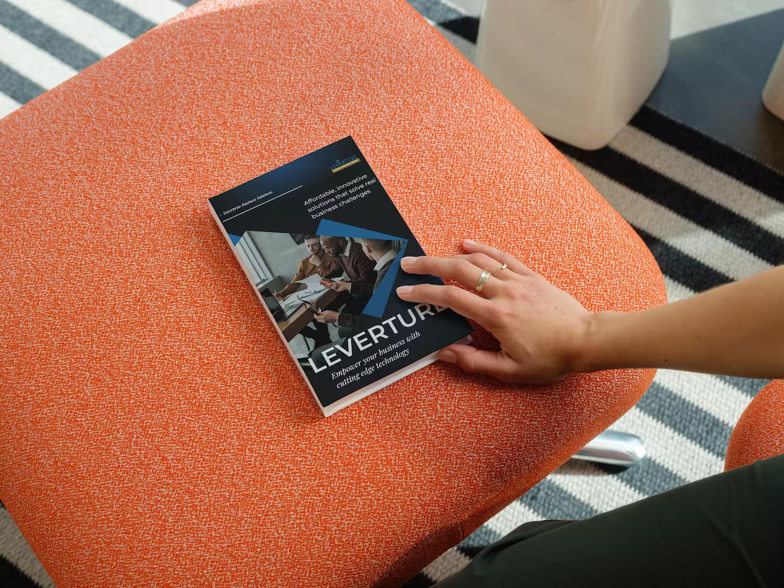 Printed Leverture conference brochure resting on an orange fabric chair with a striped black and white rug in the background