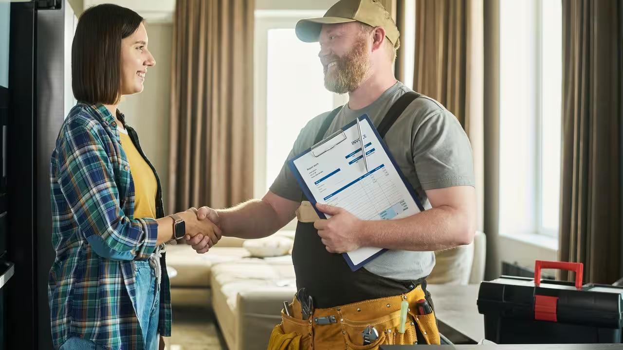 A repair technician finishing up with a homeowner in her kitchen, the moment at job completion when the review should be asked for in person.