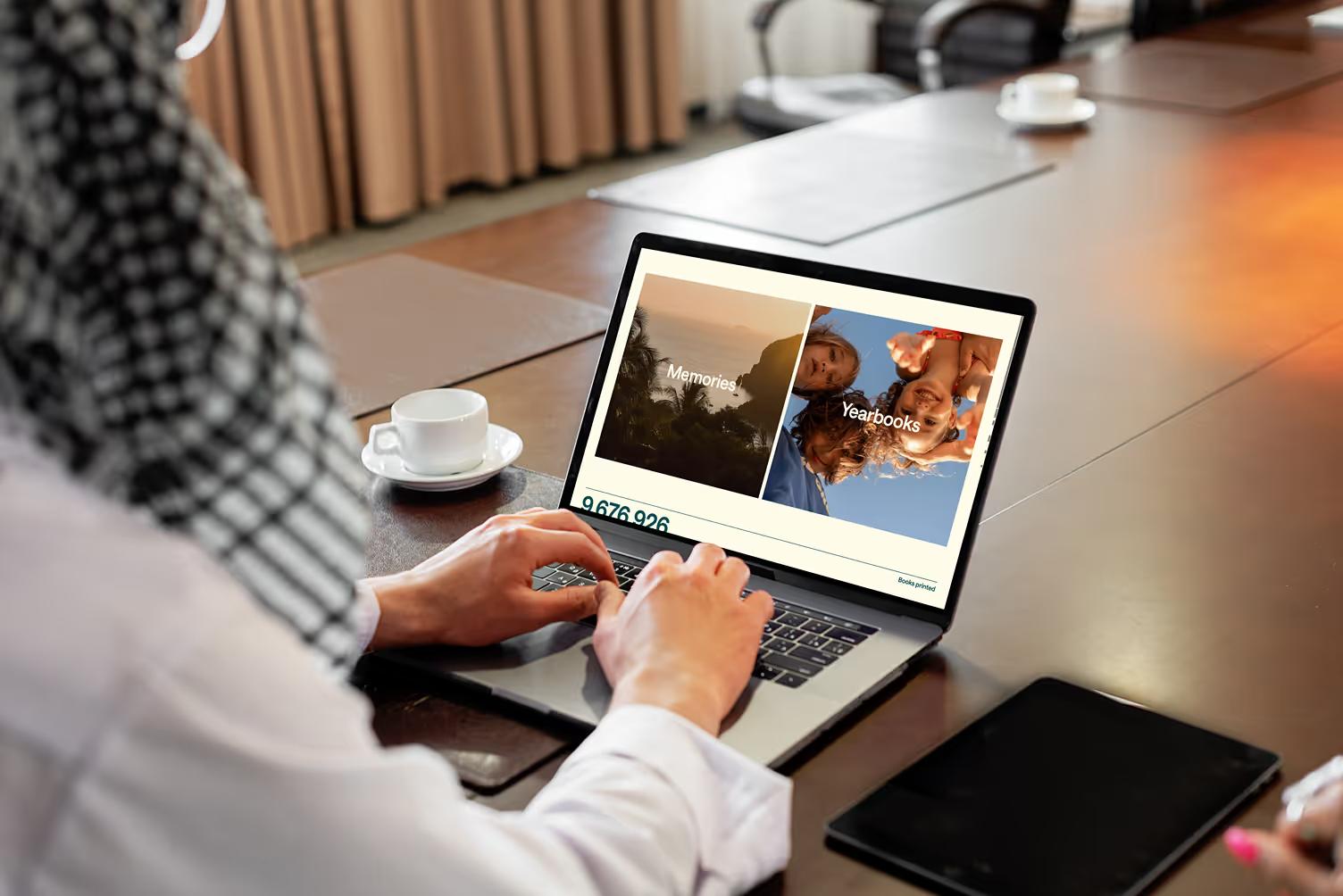 Person at conference table browsing TreeRing on MacBook showing Memories and Yearbooks section cards with animated stats counter displaying 9,676,926 memories