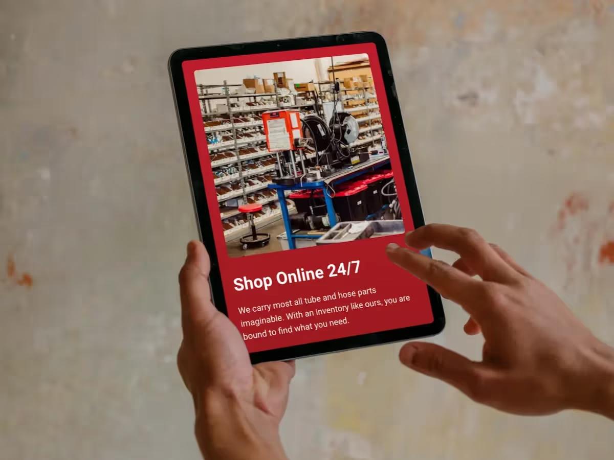 Hands holding a tablet showing the Fluid Line Solutions Shop Online 24/7 section with a photo of the hose and fittings shop