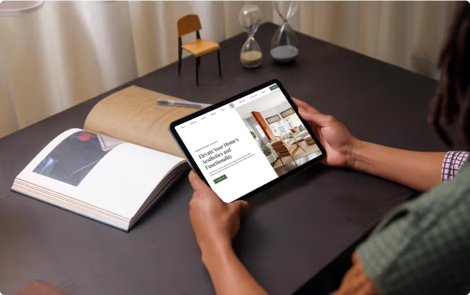 Person holding iPad at desk browsing Circle T Specialties residential page showing Elevate Your Home headline with interior window treatment photos