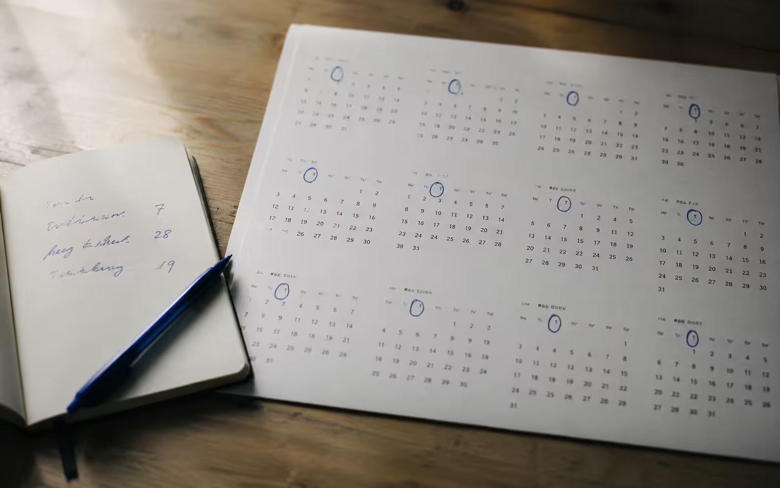 A wall calendar with the first Tuesday of each month circled next to an open notebook tracking three numbers.