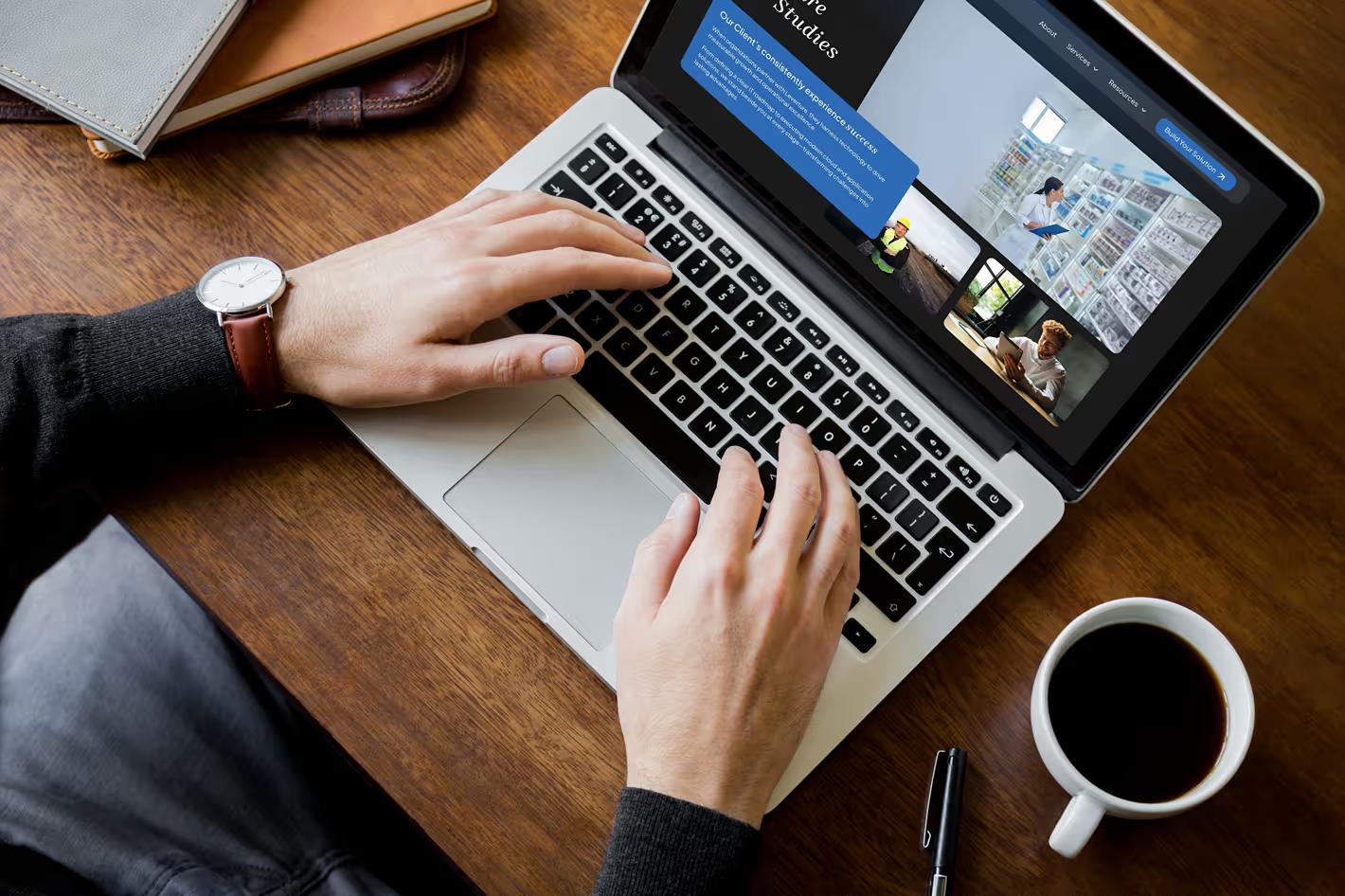 Person typing on MacBook laptop displaying the Leverture case studies page, photographed from above on a wooden desk with coffee cup and pen