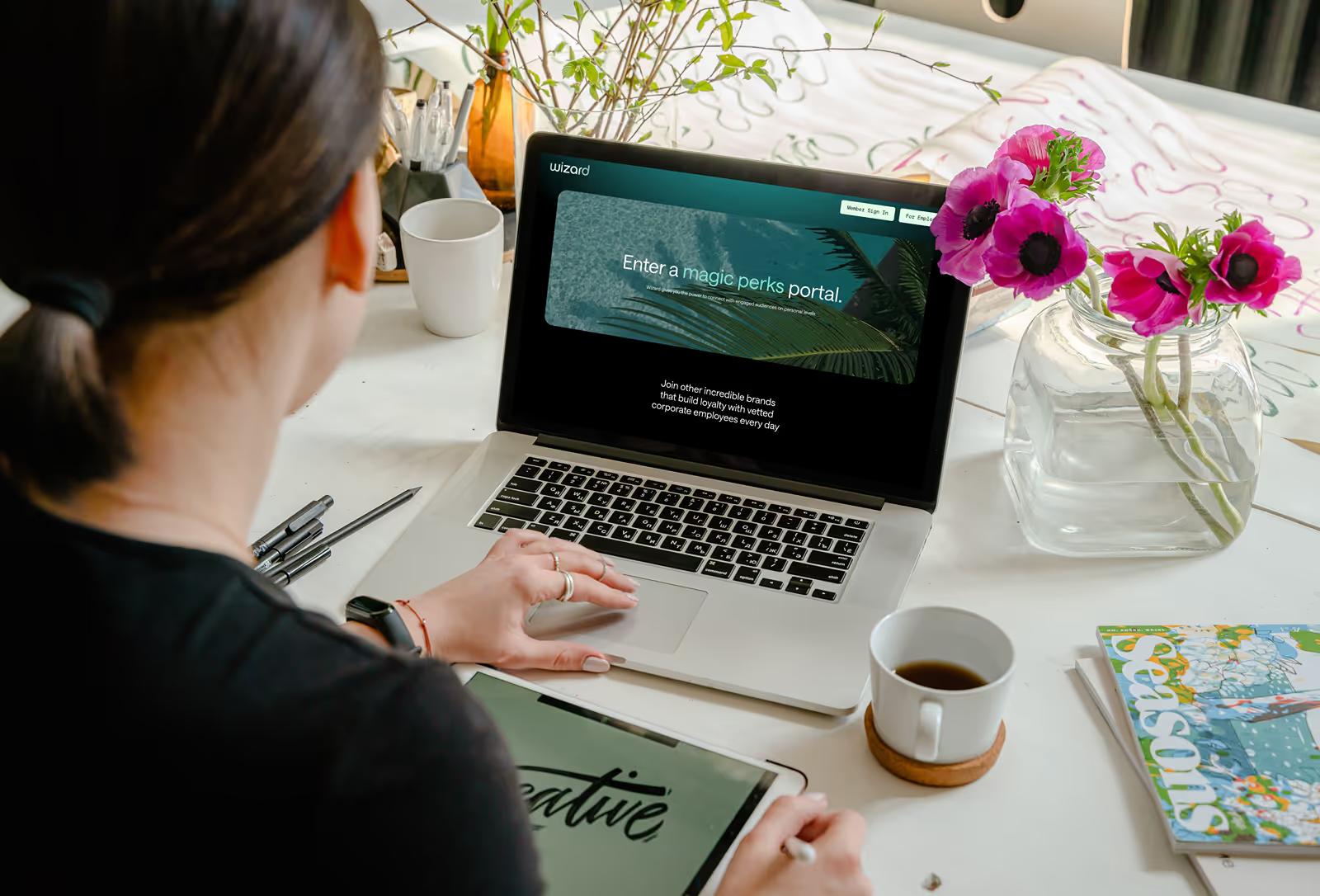 Woman browsing Wizard Perks hero page on MacBook at creative workspace