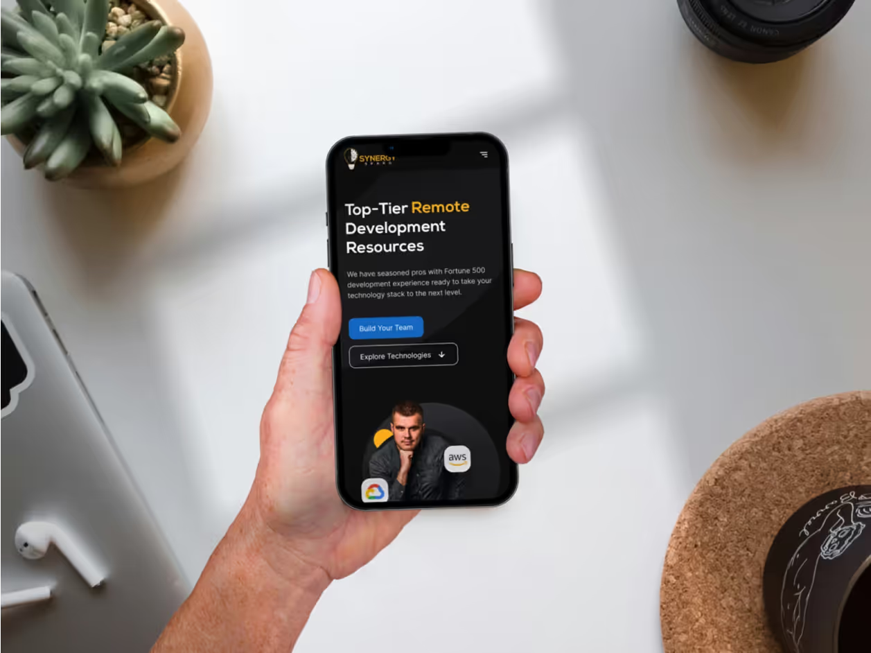 Hand holding iPhone showing Synergy Sparq mobile homepage with Top-Tier Remote Development Resources headline, Build Your Team CTA, and developer photo with AWS and Google Cloud badges
