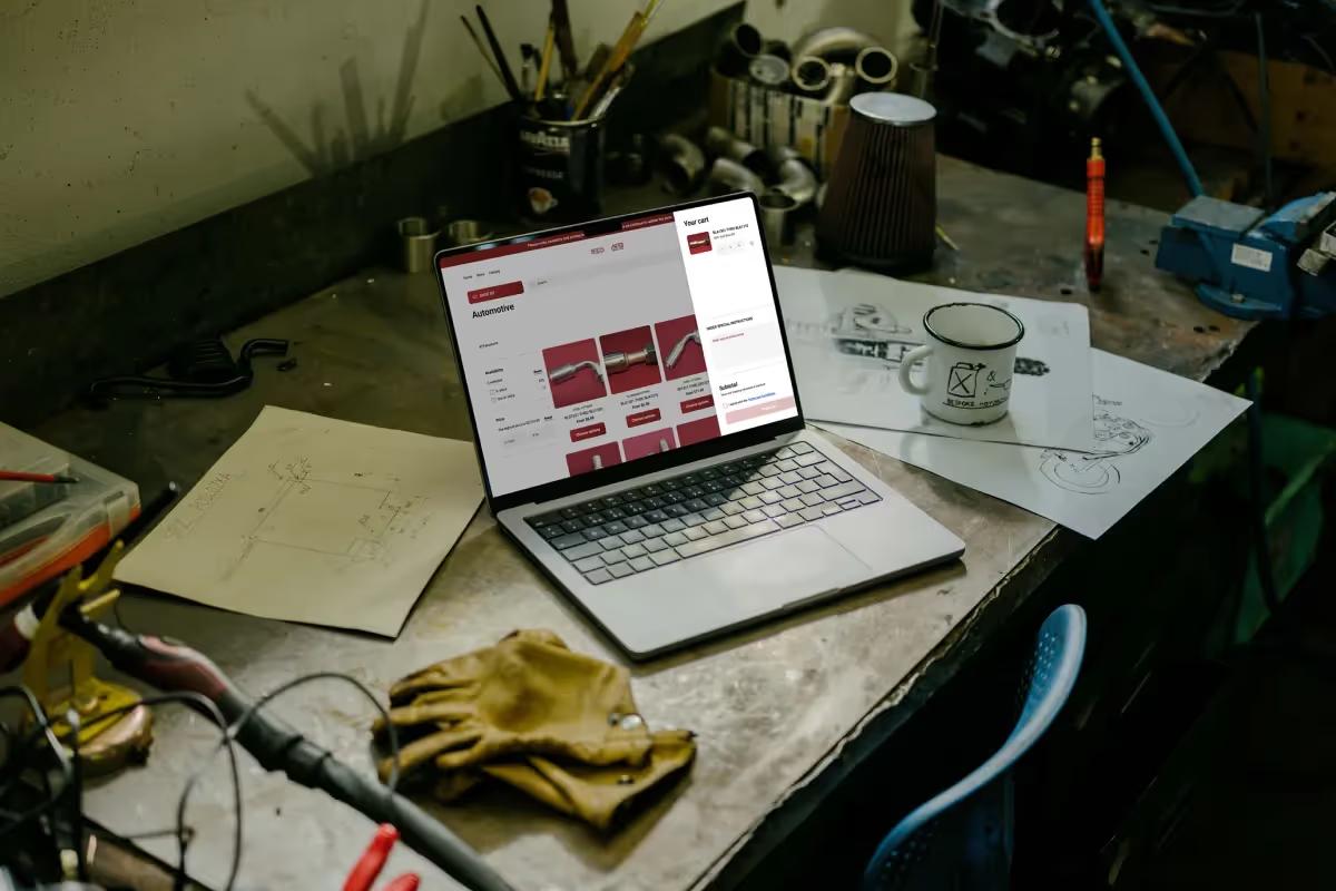 Laptop on a workshop bench showing the Fluid Line Solutions Shopify store automotive category with the shopping cart open