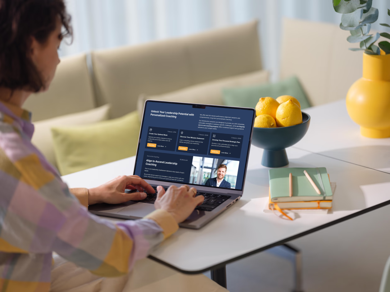 Woman at home office browsing Connally Consulting coaching services page on MacBook showing Unlock Your Leadership Potential headline with service cards and coaching overview
