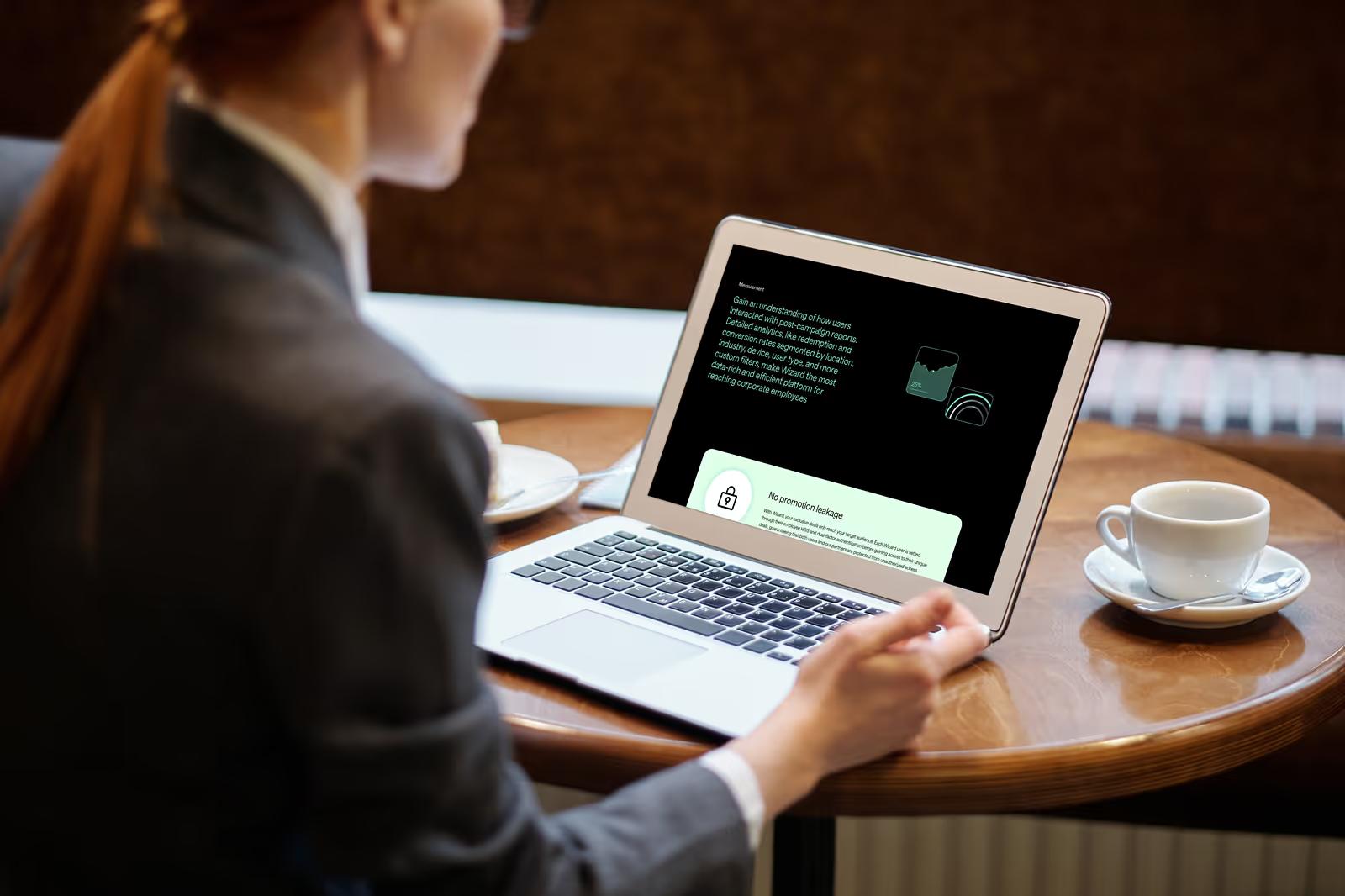 Woman at coffee shop browsing Wizard Perks merchants page showing deal cards on laptop