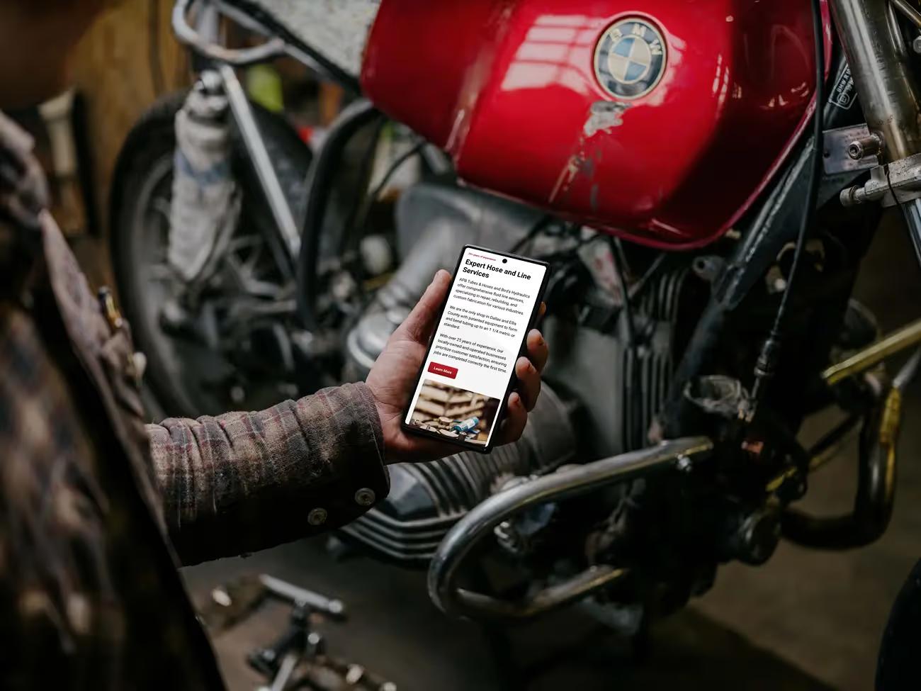 Hand holding a phone in front of a red motorcycle, showing the Fluid Line Solutions Expert Hose and Line Services section