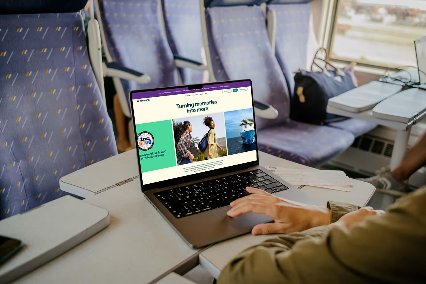 MacBook on train tray table showing TreeRing homepage hero Turning memories into more with Inc 500 badge and lifestyle photography