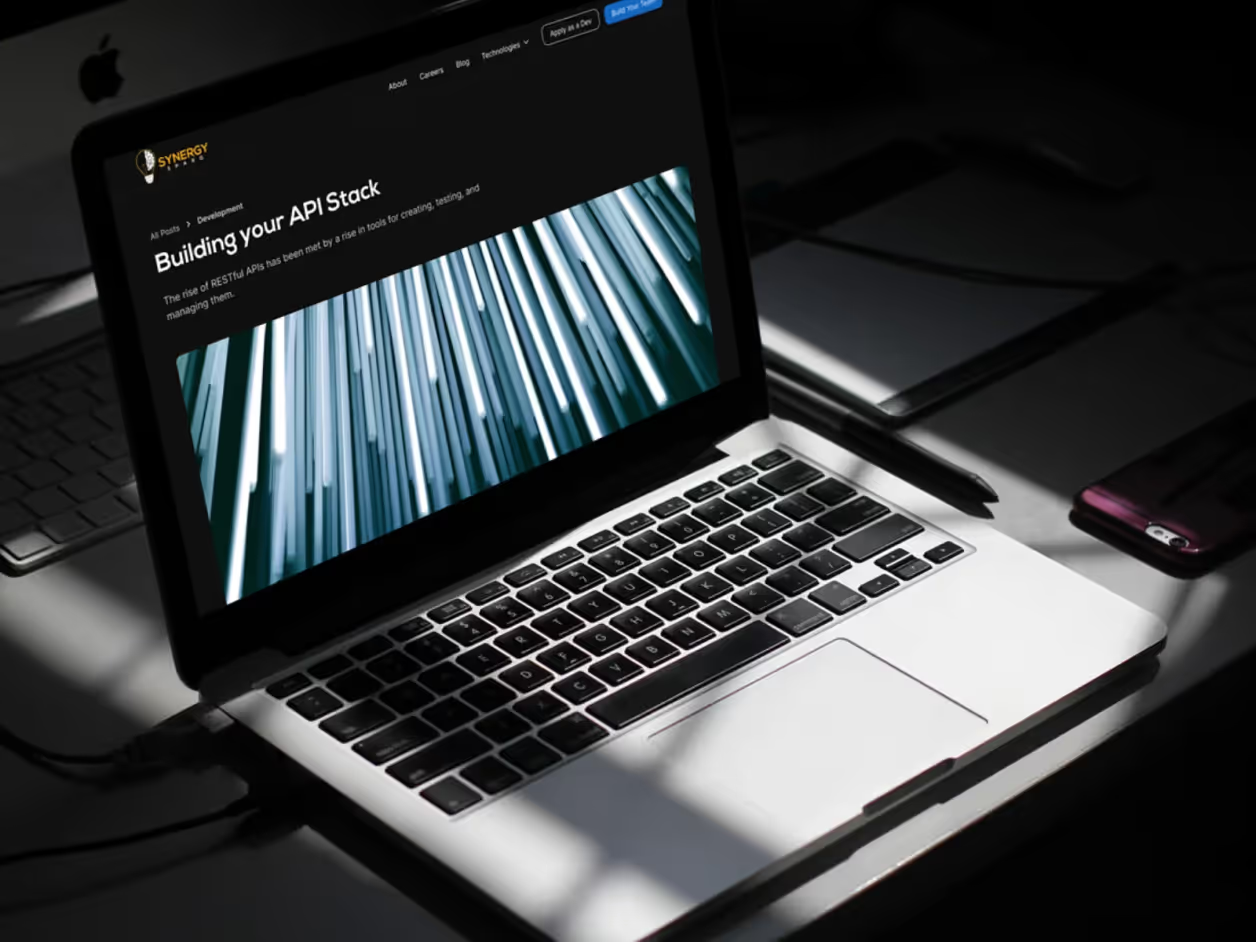MacBook in dramatic side lighting showing Synergy Sparq blog article Building your API Stack with blue abstract server imagery hero on dark-themed layout