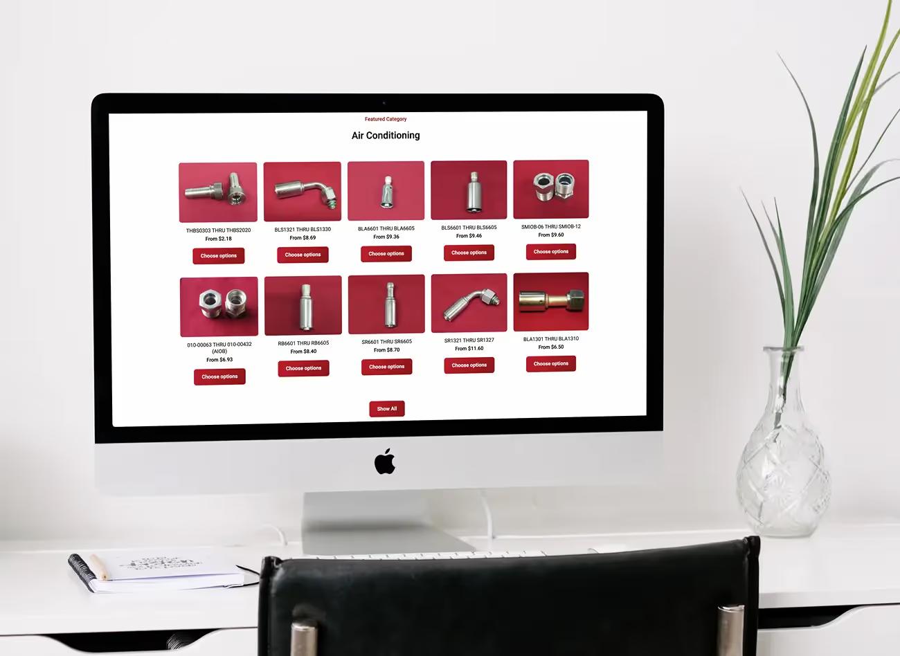 iMac on a white desk showing the Fluid Line Solutions Shopify store air conditioning fittings category with prices and Choose options buttons