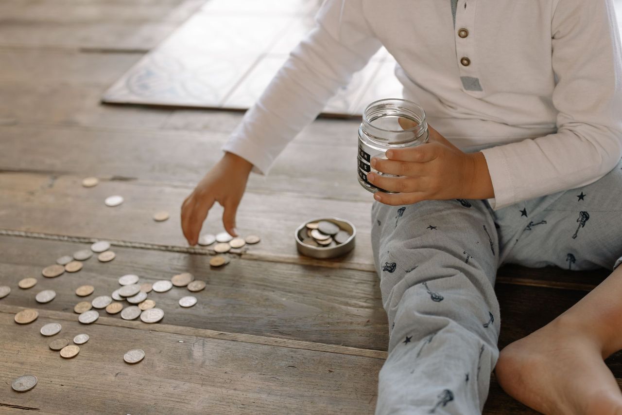 Child placing coins into labelled saving and spending containers beside a weekly family chart