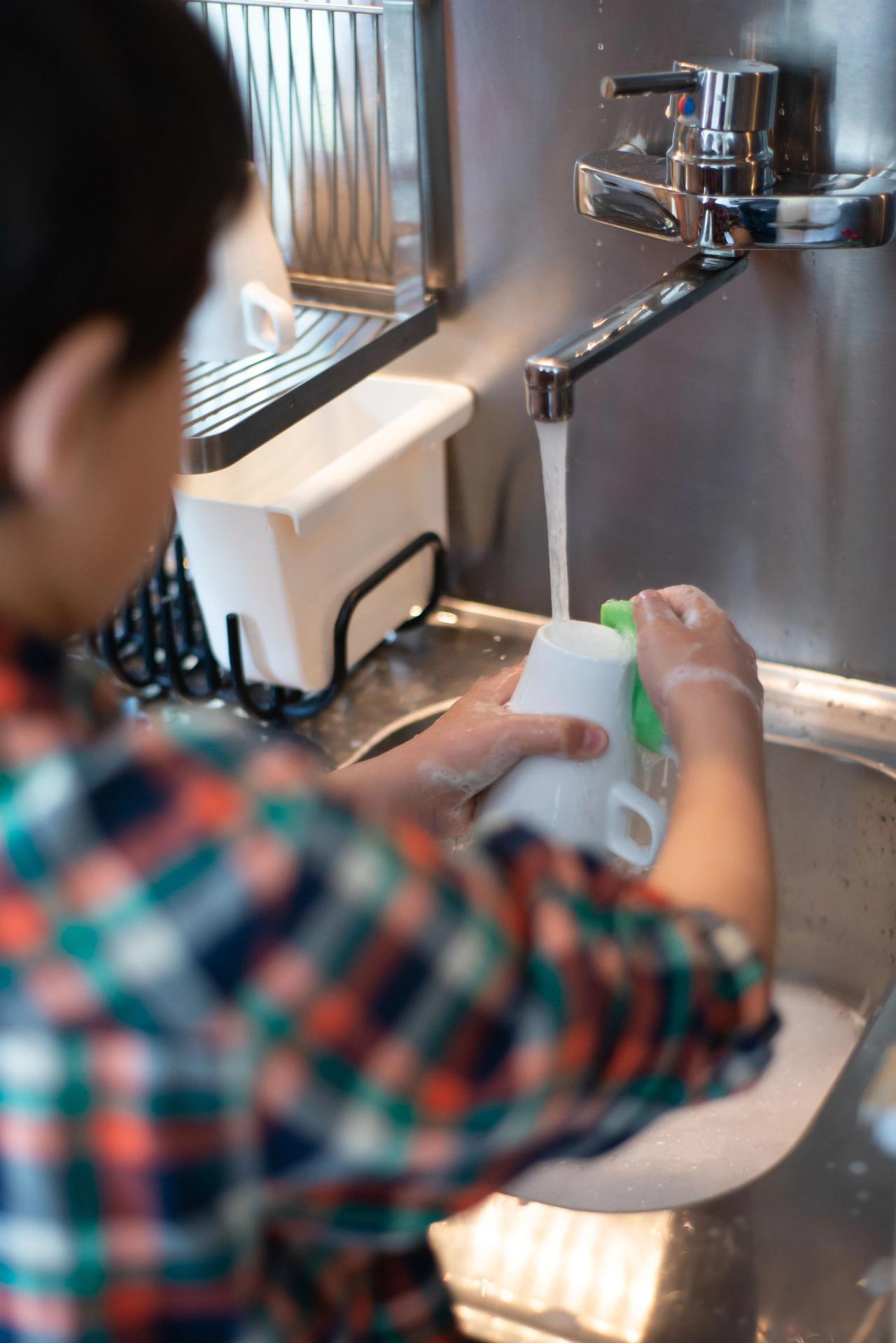 Un enfant lave une tasse dans l'évier de la cuisine