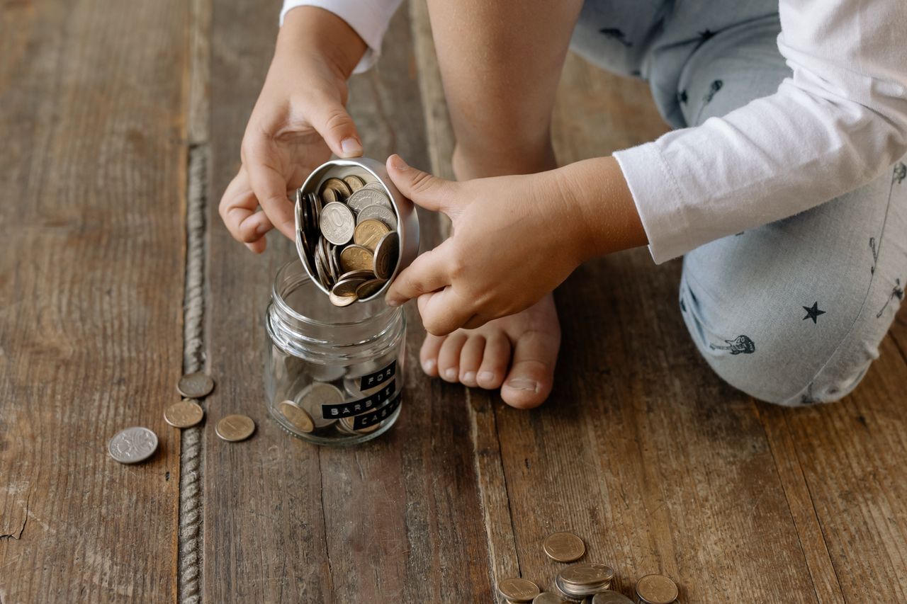 Enfant qui verse des pieces dans un bocal etiquete au nom de ce qu'il veut s'offrir