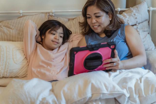 Une mère et sa fille regardent ensemble l'écran d'une tablette dans un salon 