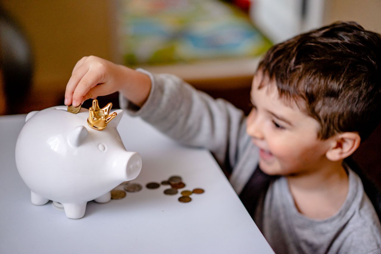 Enfant souriant qui glisse une piece dans sa tirelire, des pieces posees sur la table