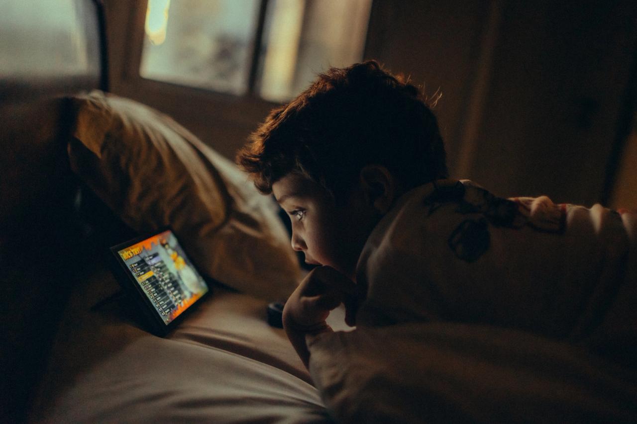 Un enfant regarde une tablette dans une chambre faiblement éclairée, le soir