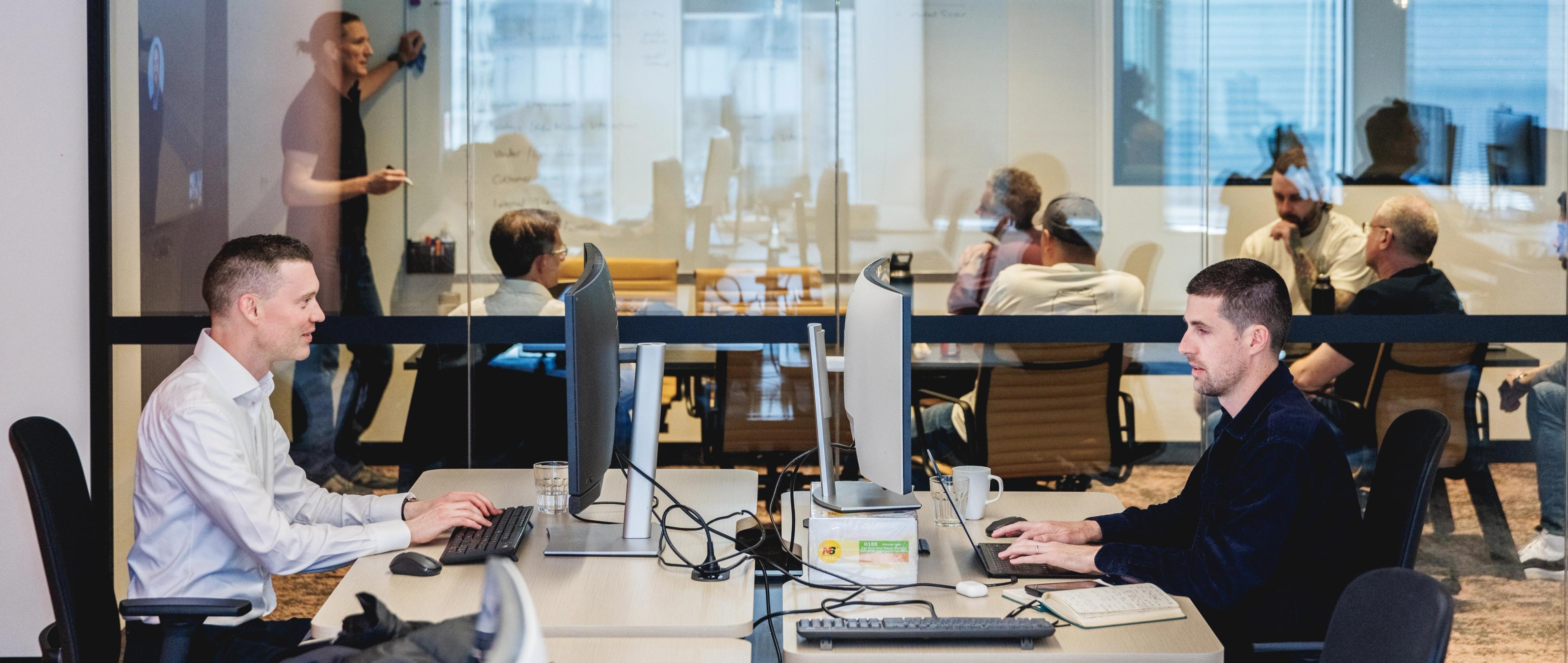 a group of men are sitting at desks in an office working on computers .