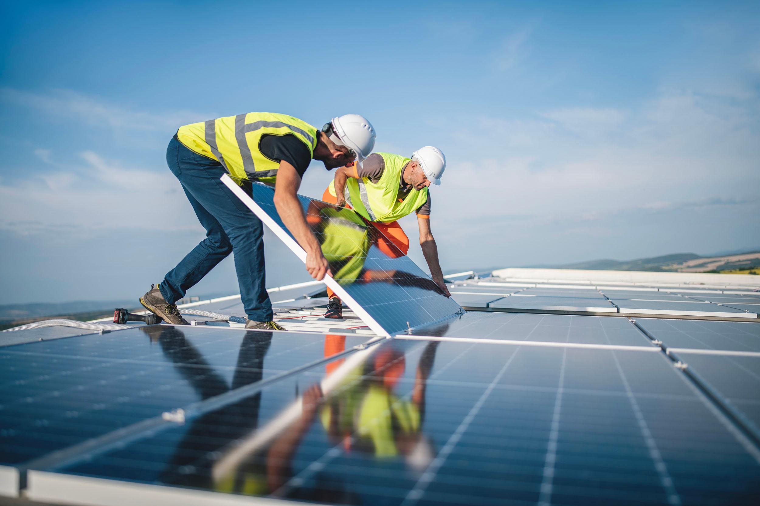 two men are installing solar panels on the roof of a building .