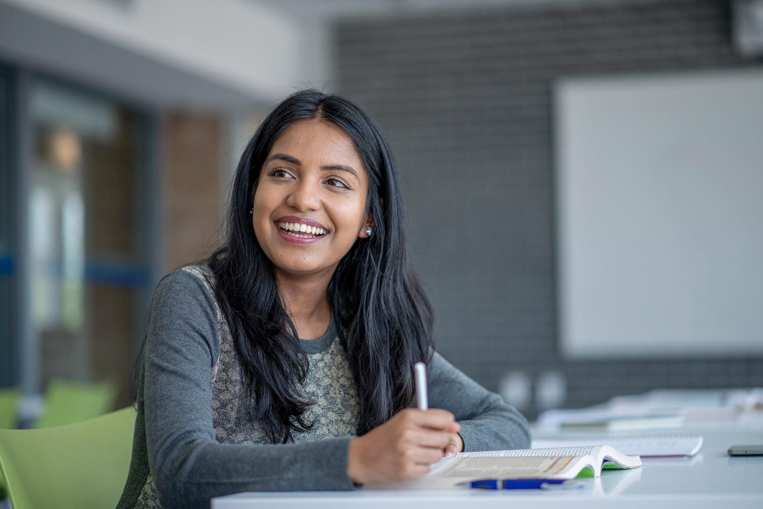 a woman is smiling while sitting at a desk in a classroom .