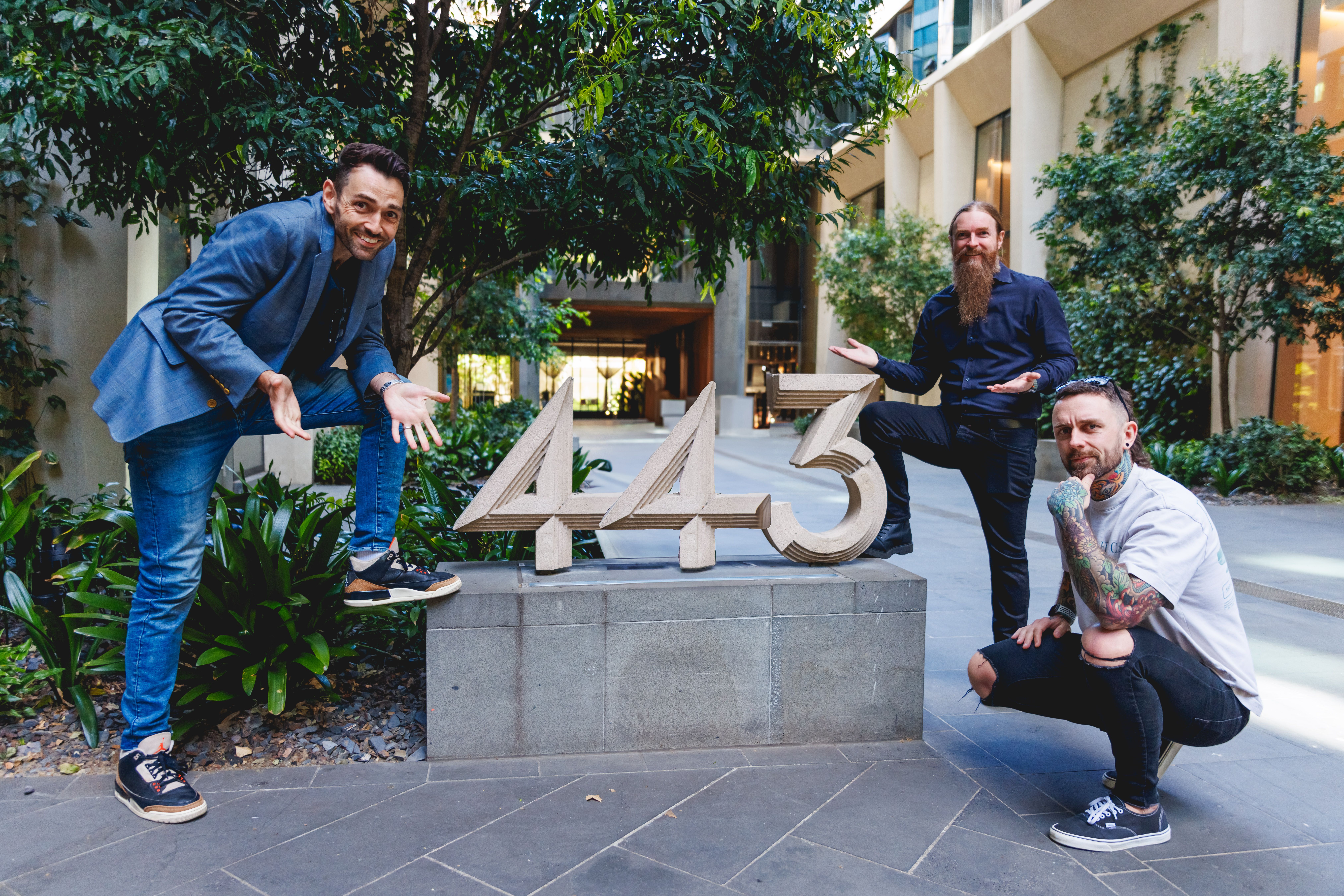 three men are posing for a picture in front of a sign that says 443 .