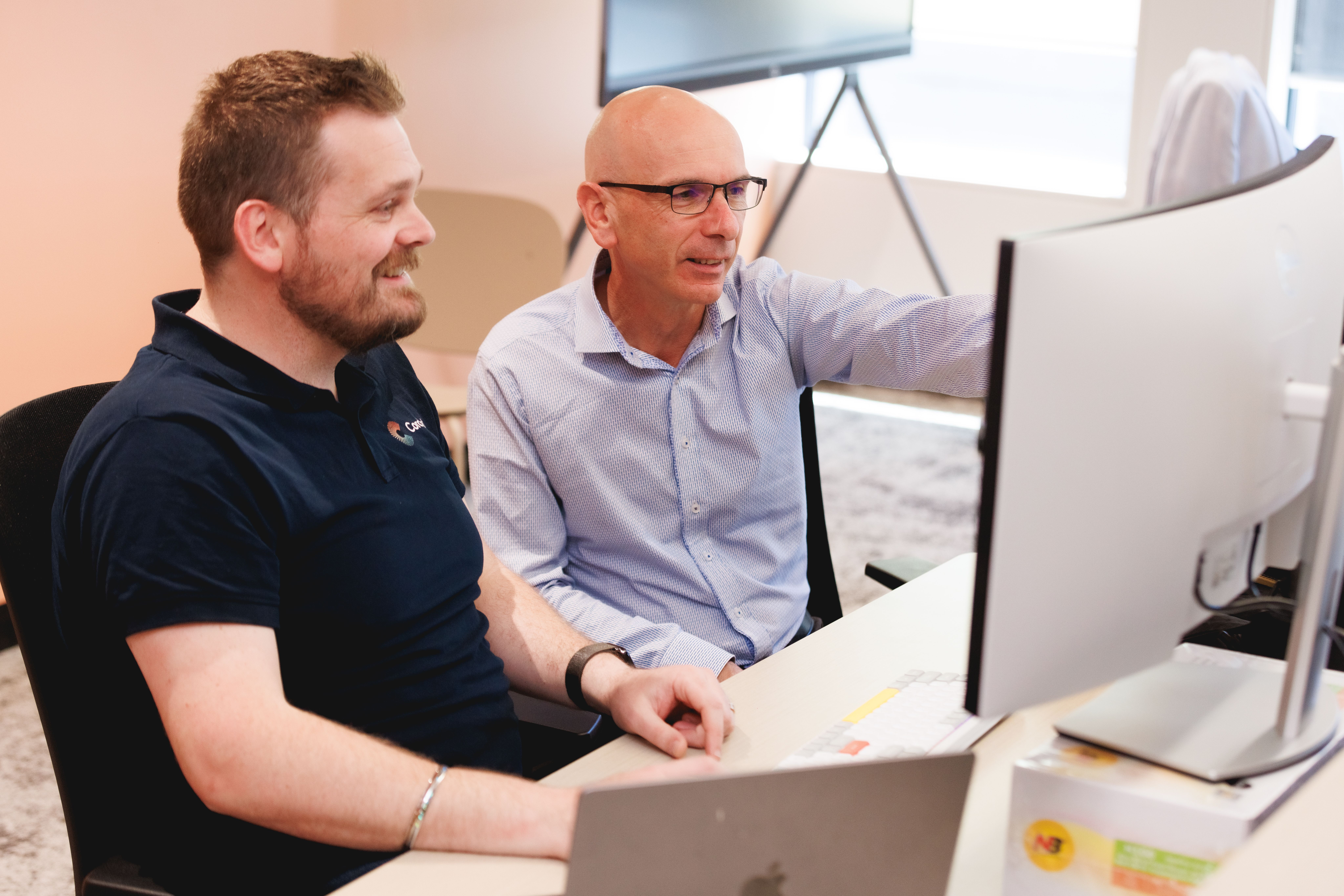 two men are sitting at a desk looking at a computer screen .
