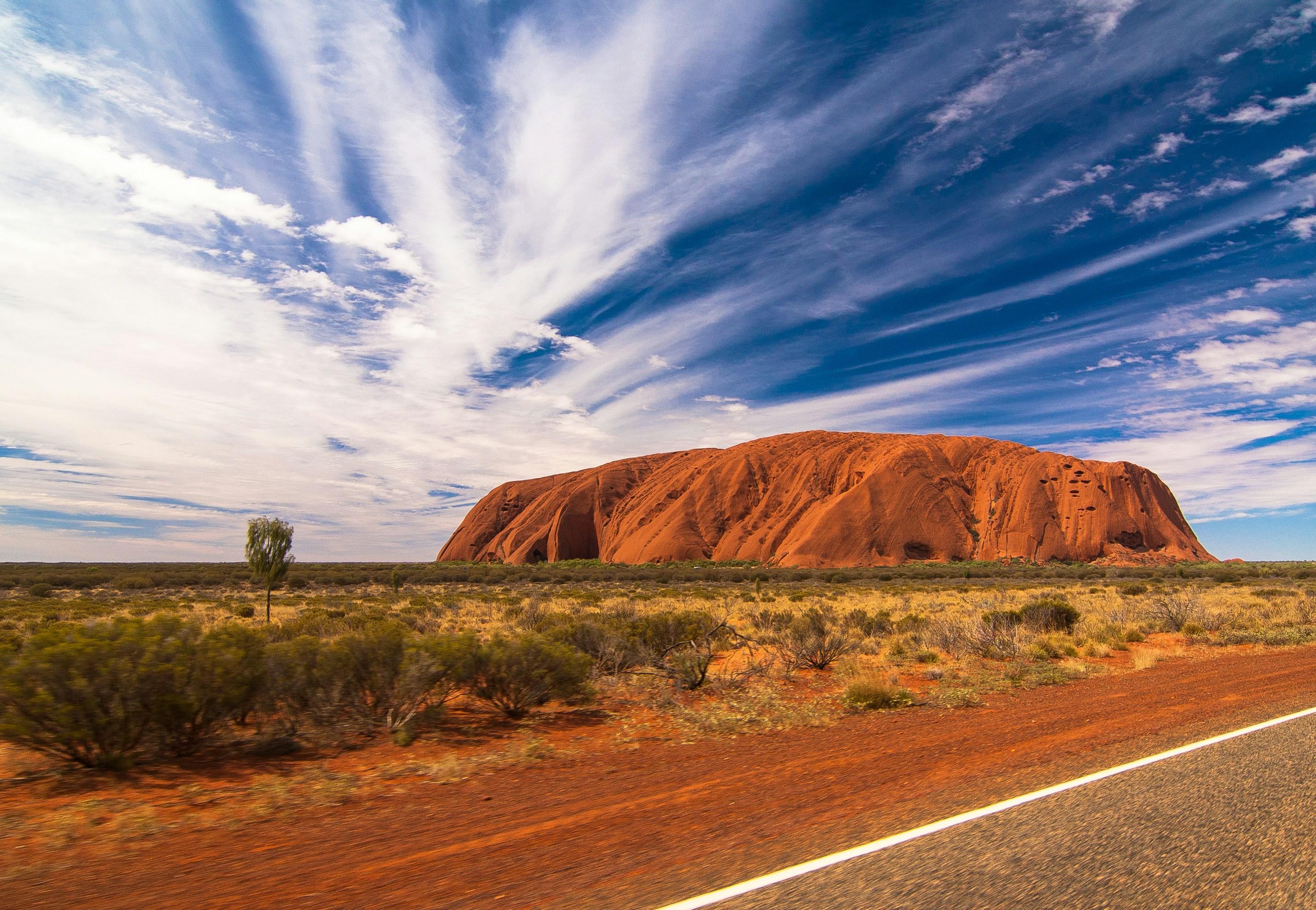 a road leading to a large rock formation in the middle of a desert .