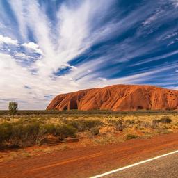a road leading to a large rock formation in the middle of a desert .