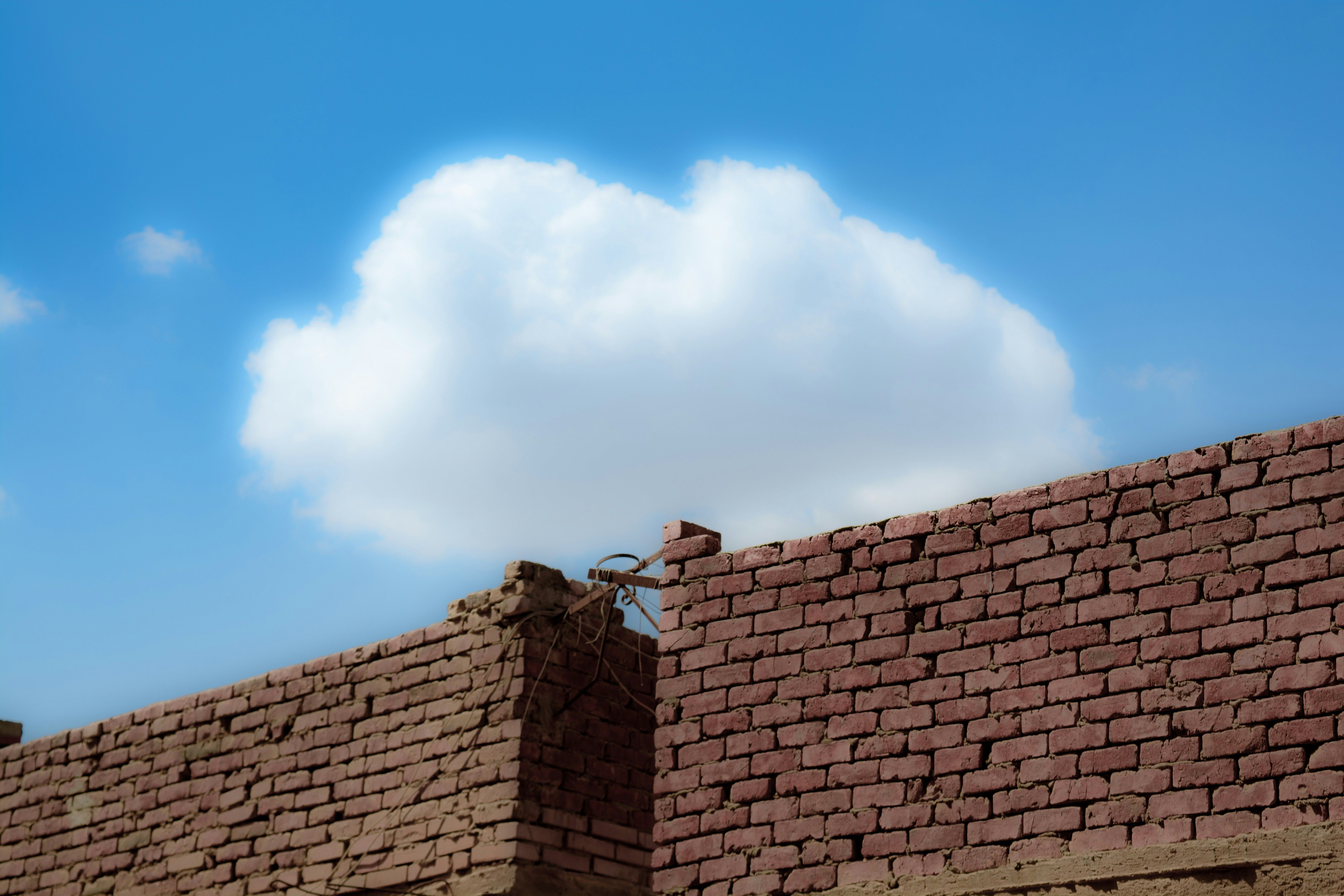 a brick wall with a cloud in the sky behind it .