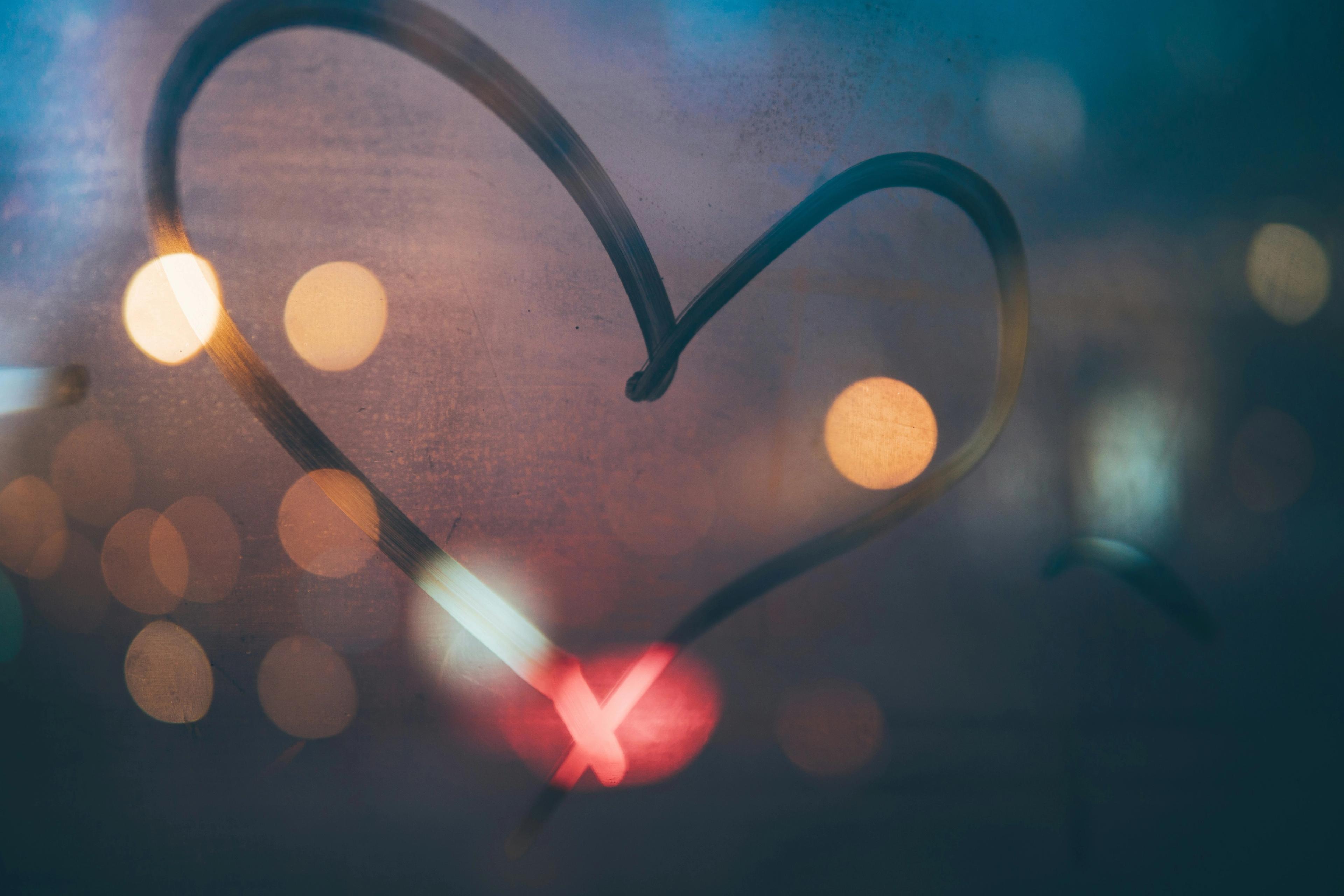 a heart is drawn on a window with lights in the background .