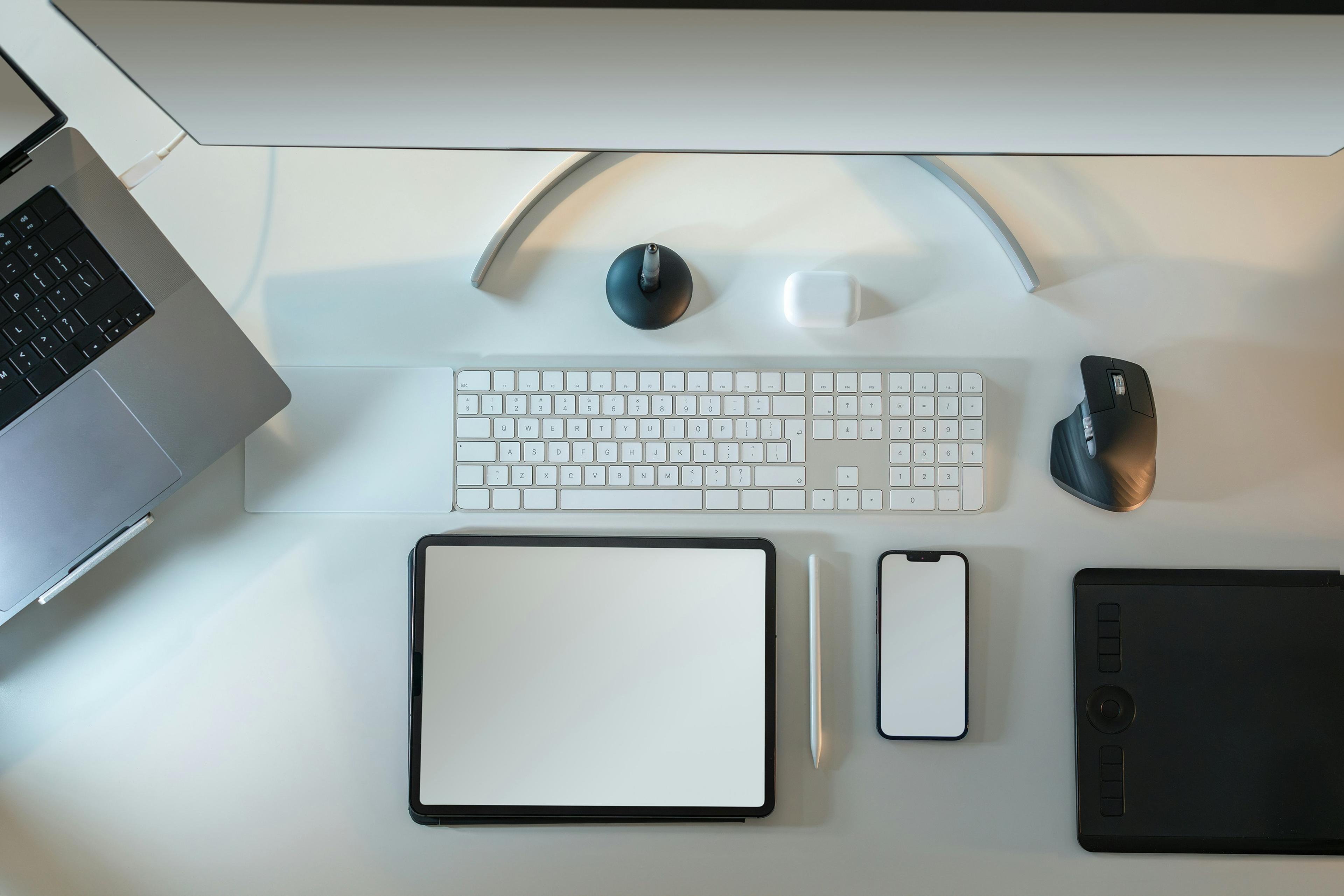 a desk with a computer , laptop , tablet , phone , keyboard and mouse .