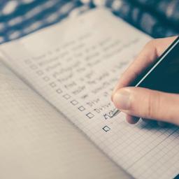 a person is writing on a checklist in a notebook with a pen .