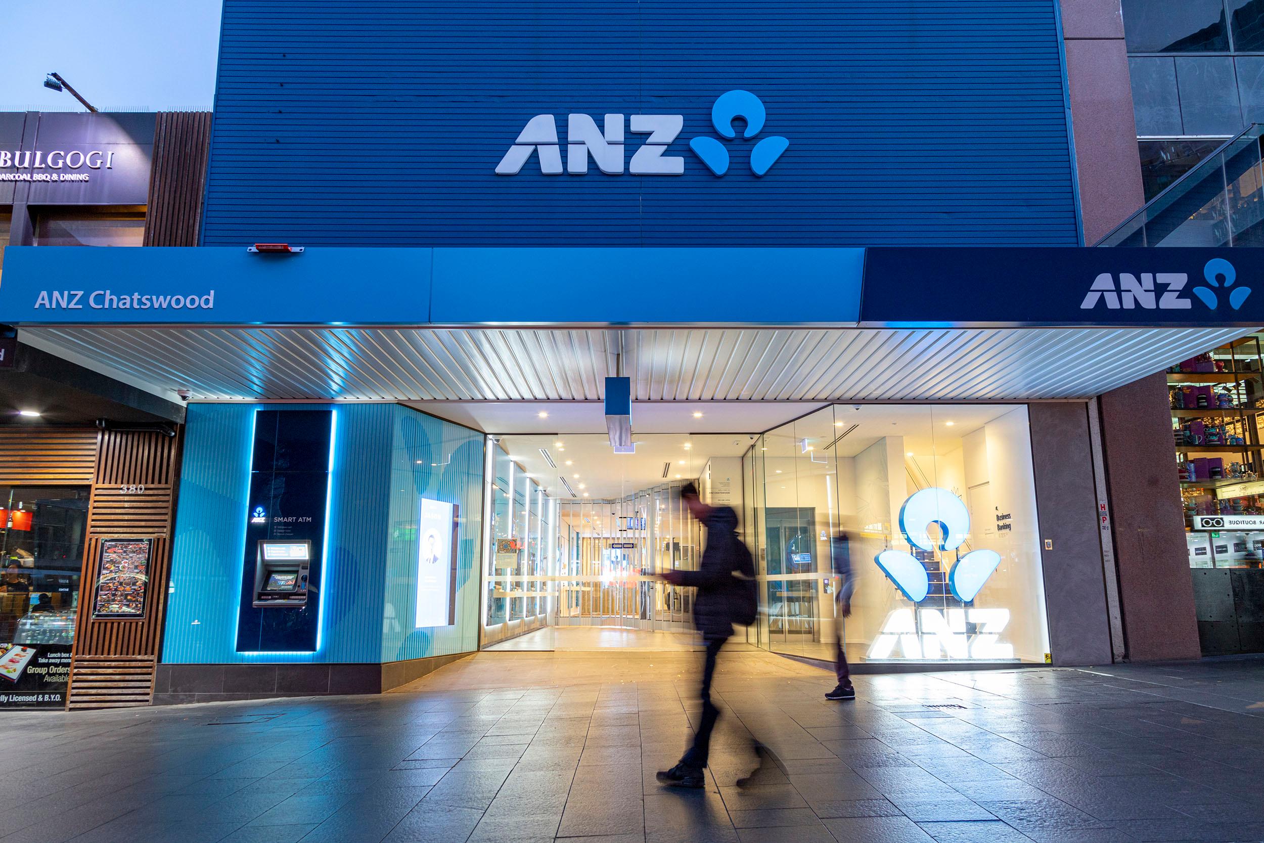 a man is walking in front of an anz bank .