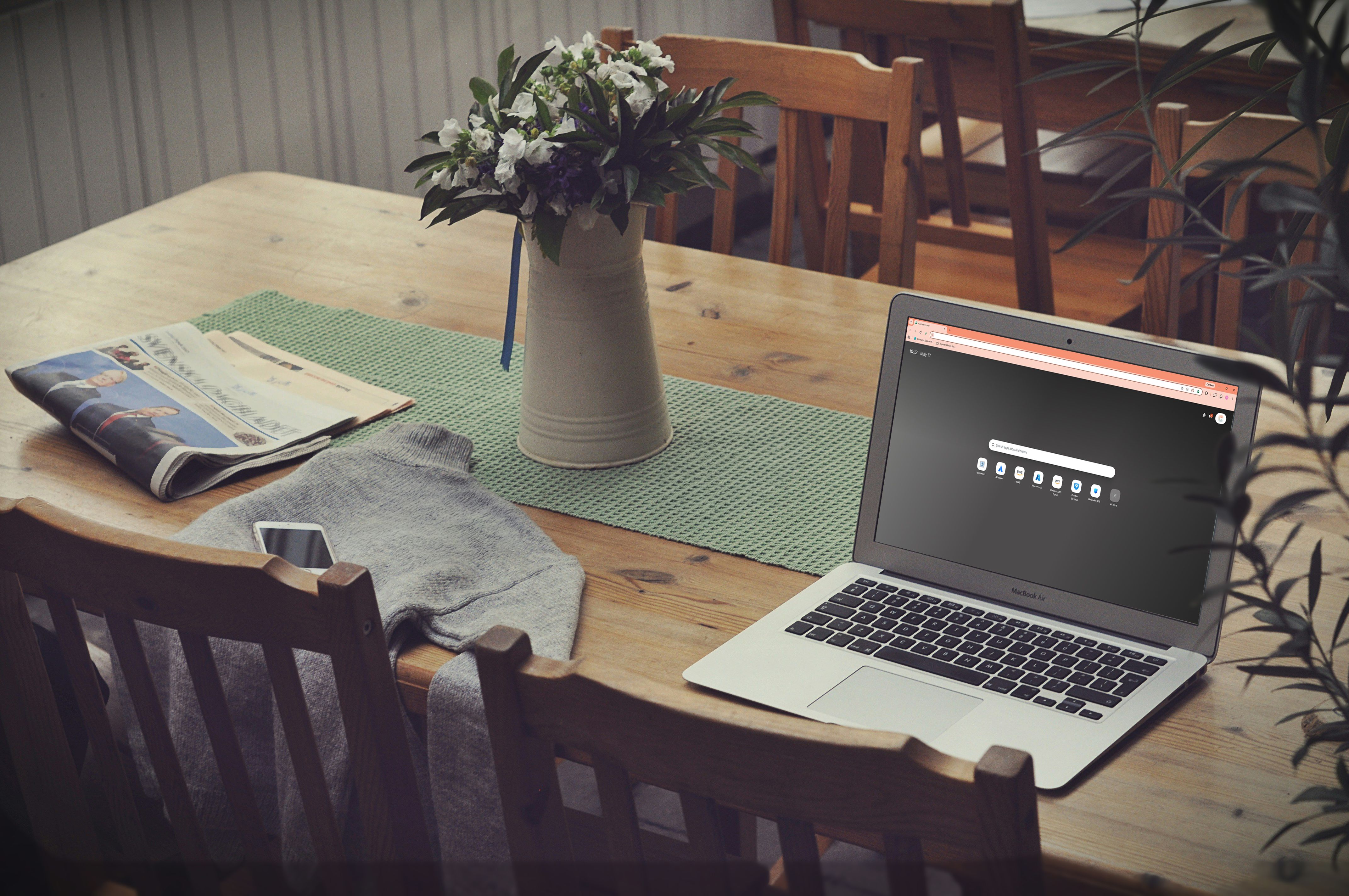 A laptop, newspaper, smartphone, and white flowers on a wooden table.
