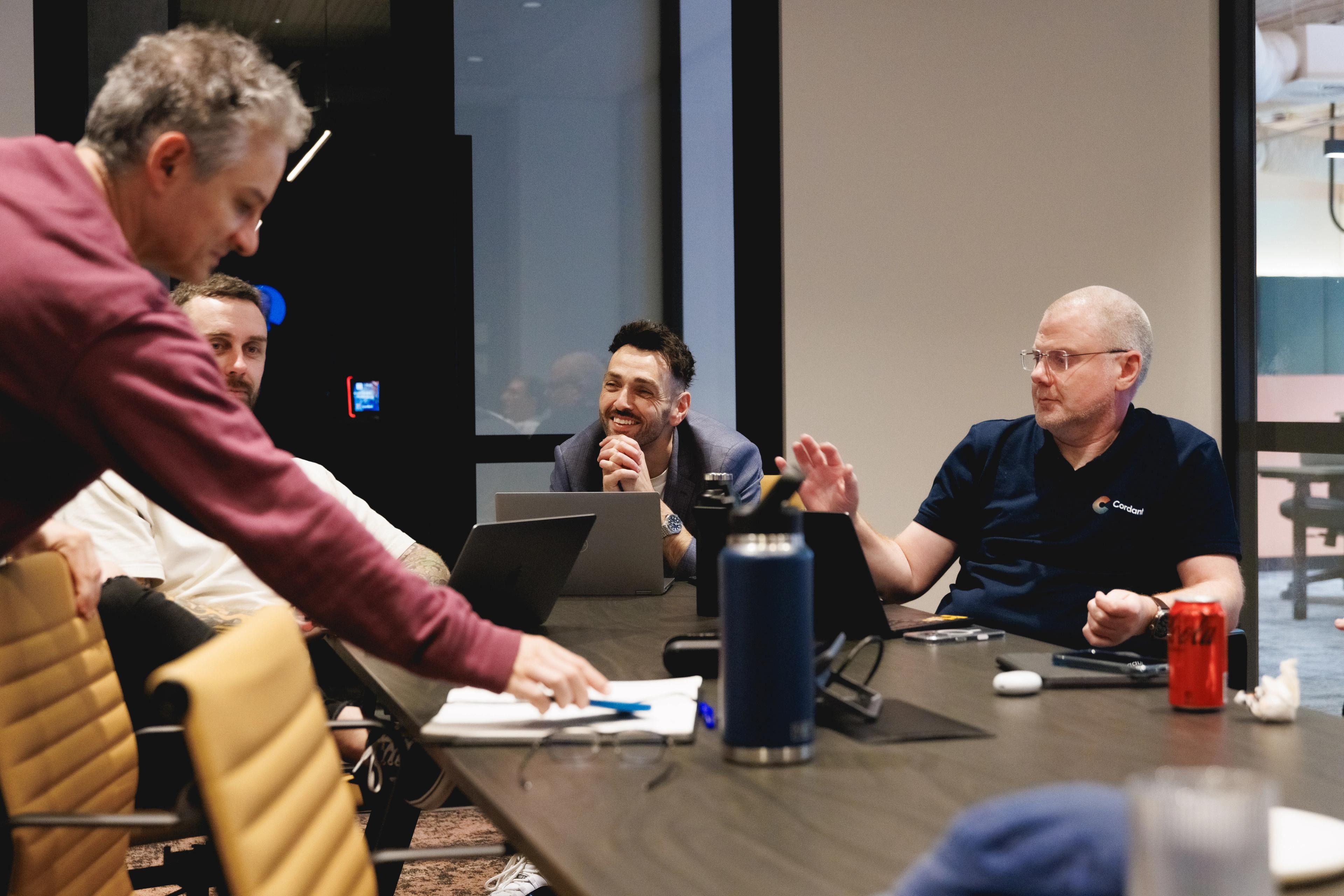 a group of men are sitting around a conference table having a meeting .