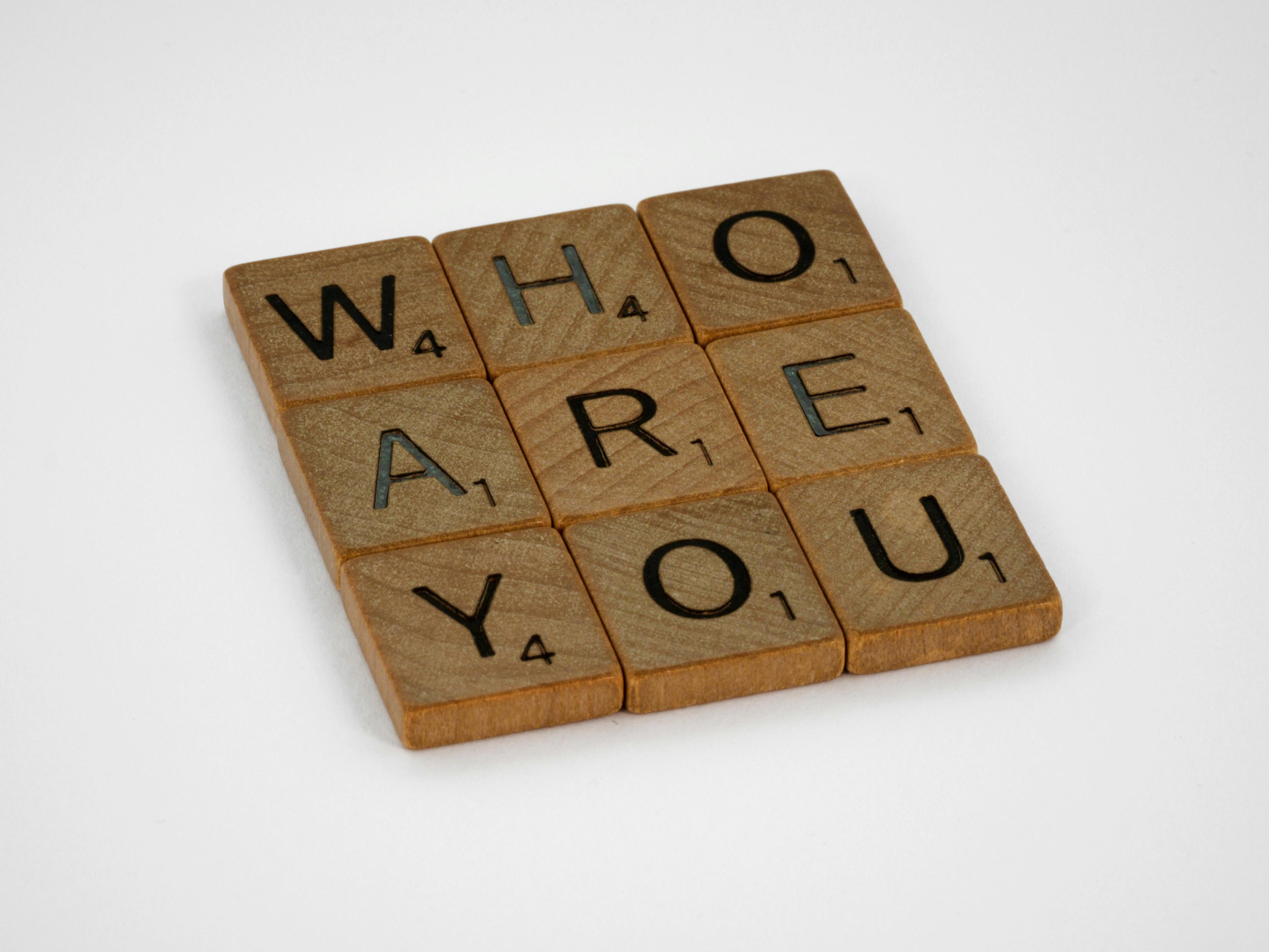 the words who are you are written on wooden scrabble tiles .