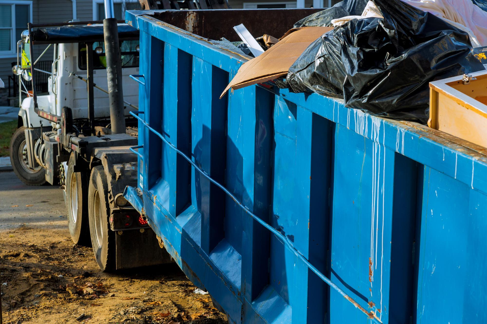 a blue dumpster is sitting next to a white dump truck .