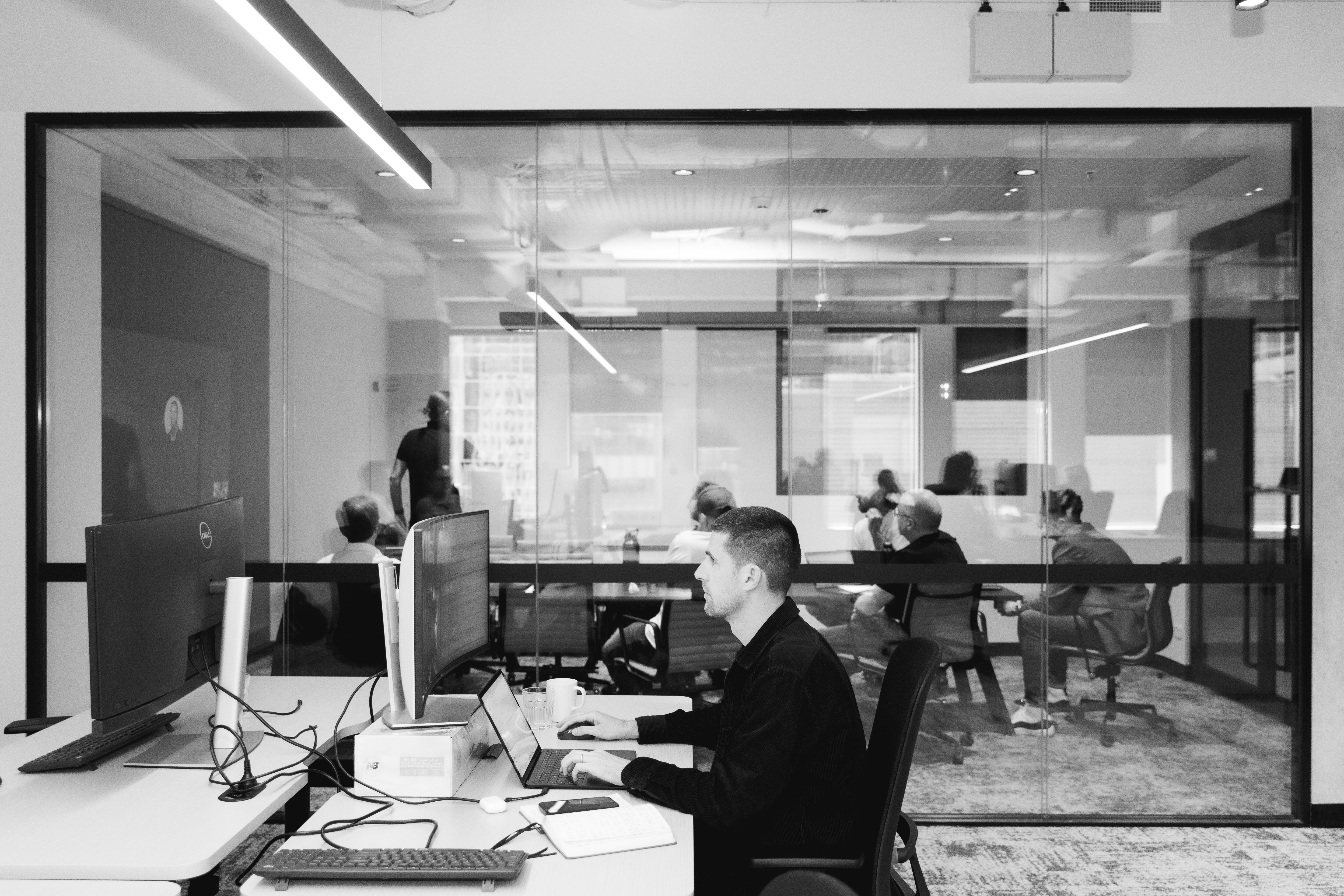 a man is sitting at a desk in an office using a laptop computer .
