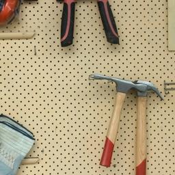 a hammer , pliers , gloves , and screwdrivers are hanging on a peg board .