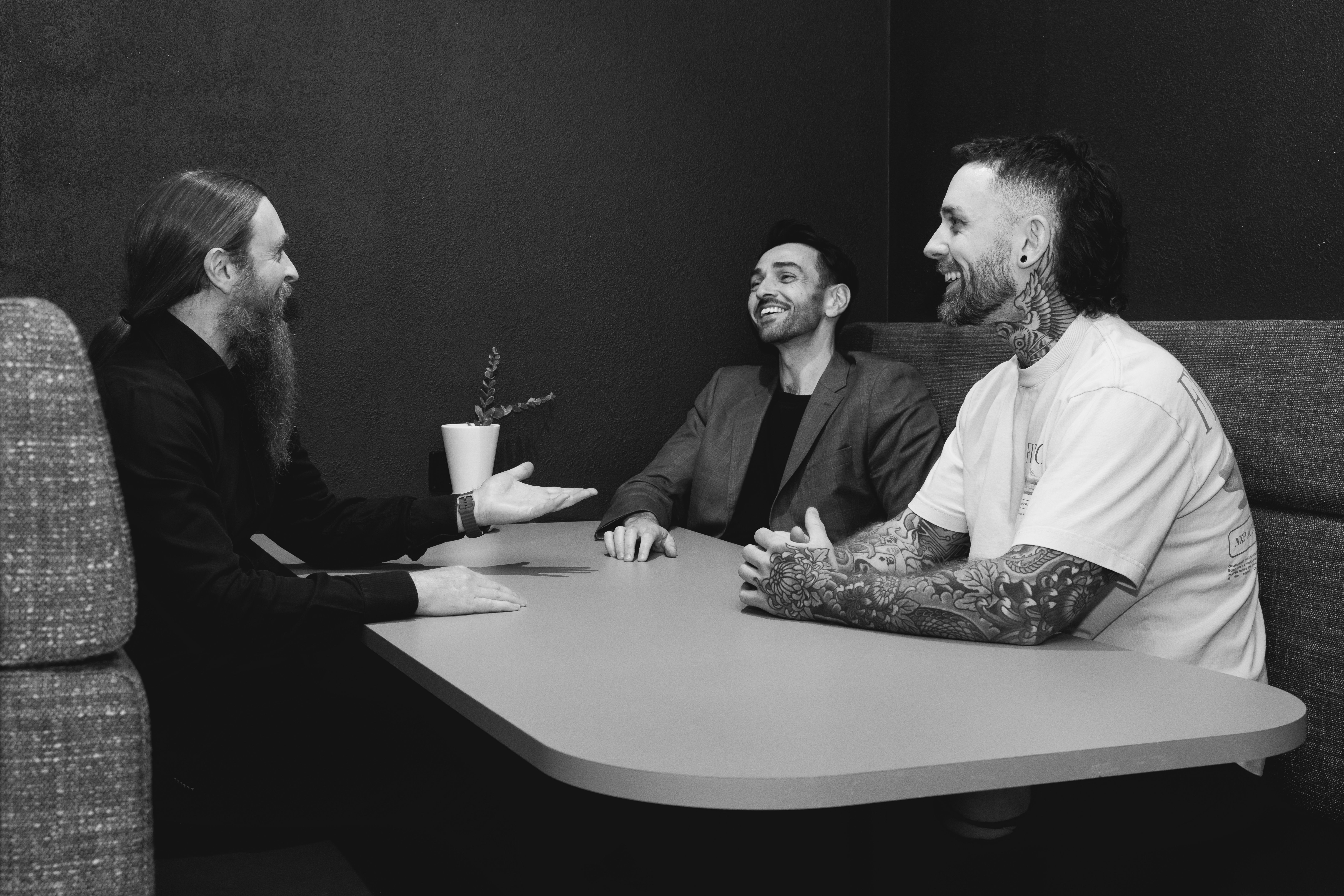 three men are sitting at a table talking to each other in a black and white photo .