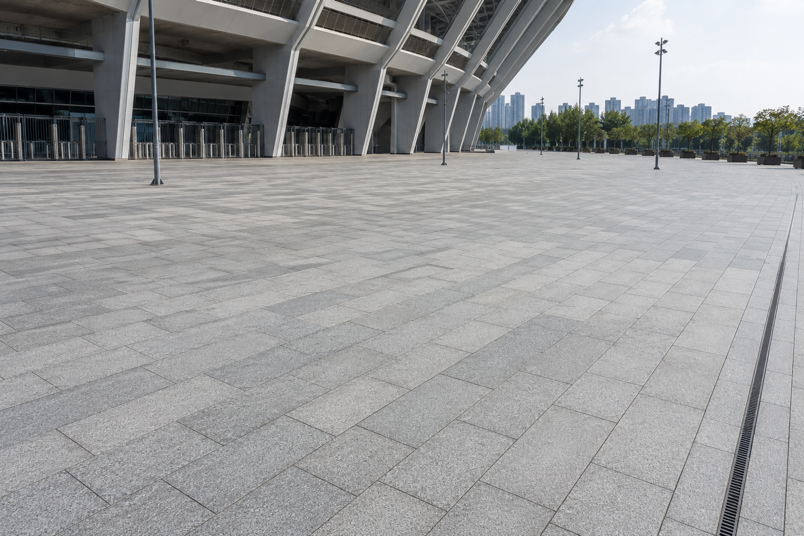Custom grey natural granite slabs paving a large stadium entrance plaza with integrated linear drainage and open event circulation space