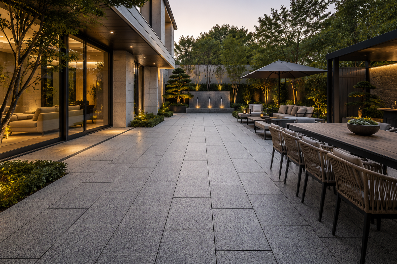 Maßgefertigte hellgraue Naturgranitplatten in einem modernen Innenhof und auf der Terrasse, die Innen- und Außenräume mit Ess-, Lounge- und begrünten Gartenbereichen verbinden.