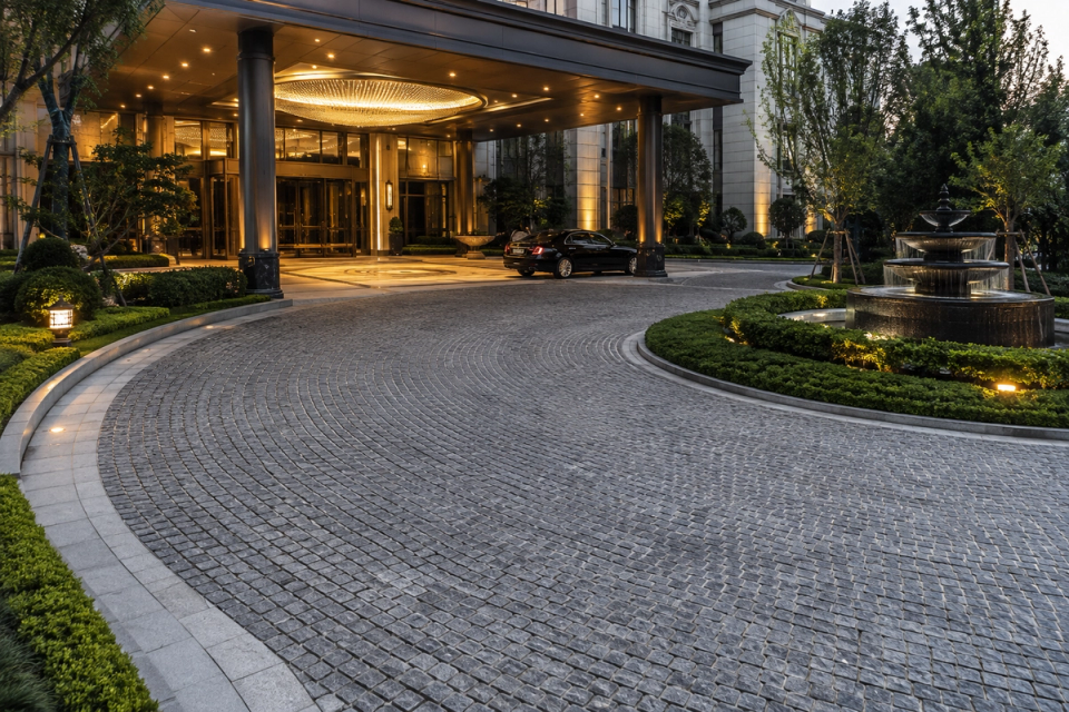 Luxury hotel entrance drop-off area and circular driveway paved with dark grey natural granite cobblestones in a curved pattern, integrated with the entrance canopy, landscaping and fountain