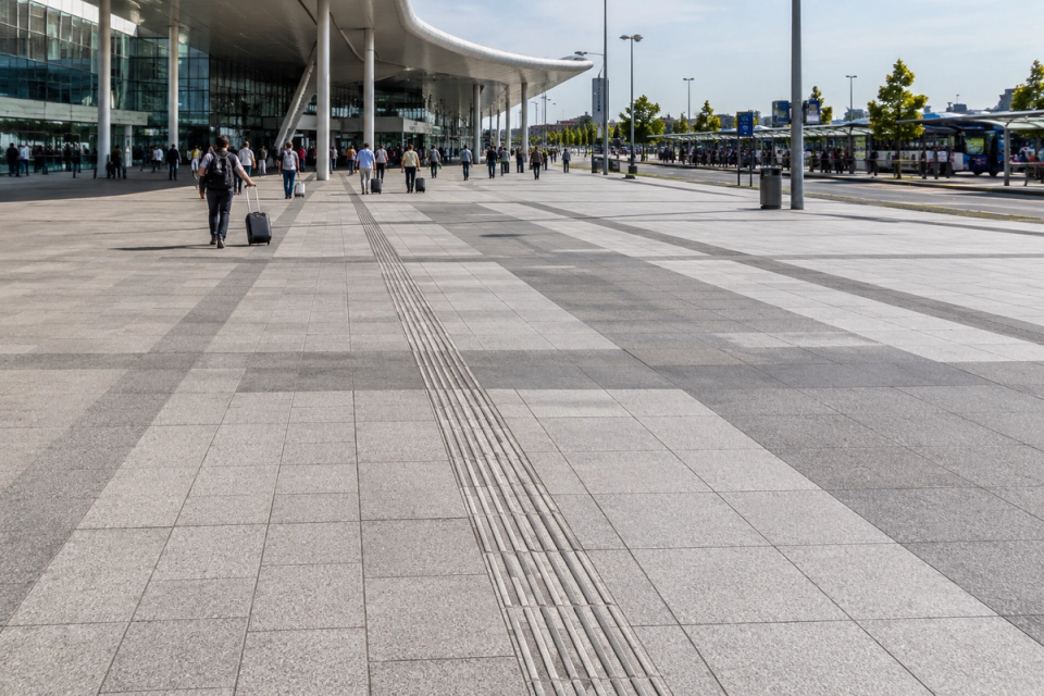 Custom granite slabs paving an urban rail station forecourt and transfer walkway, integrating large-format paving, accessible guidance and passenger circulation.
