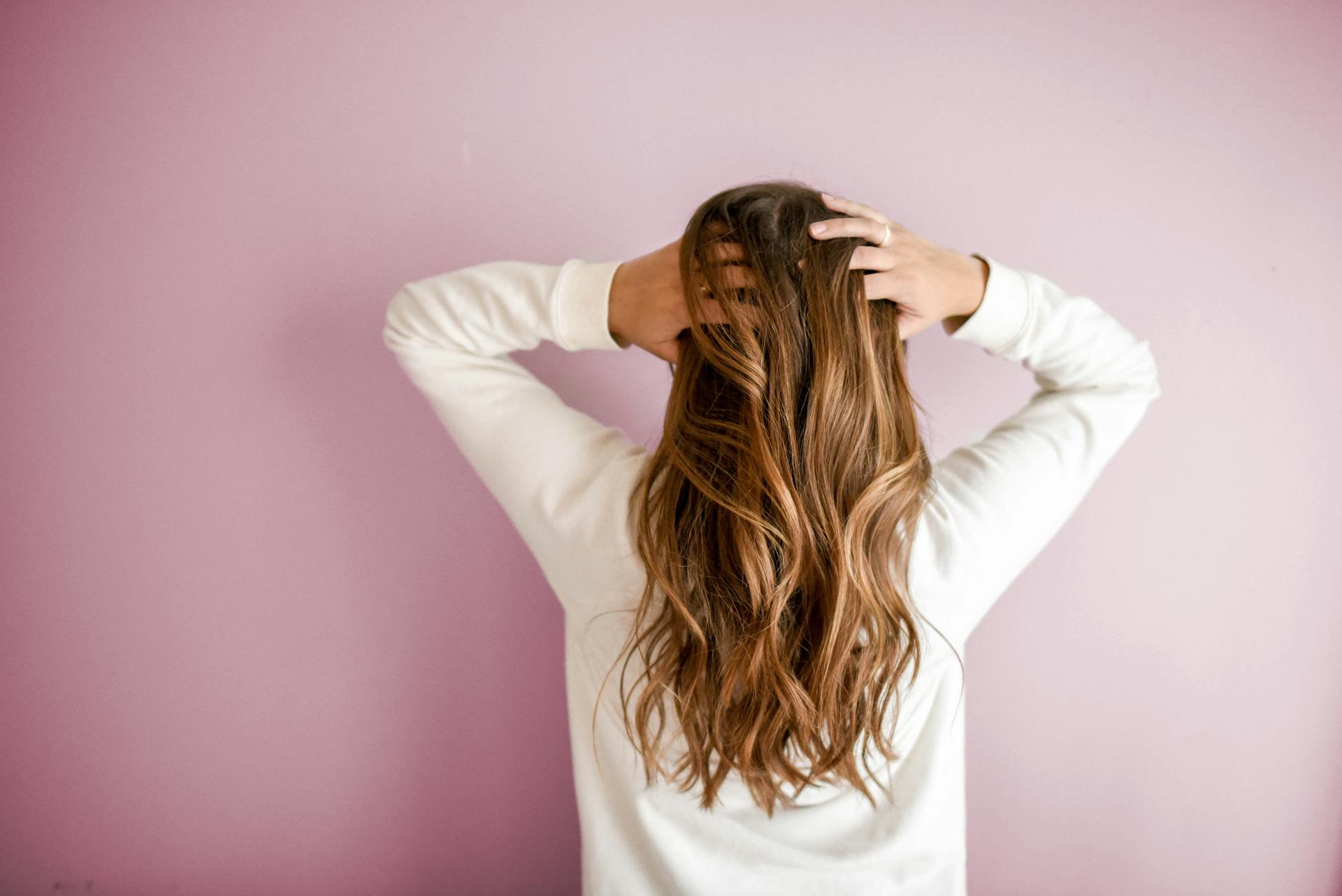 Capelli lunghi e mossi visti da dietro, su un muro rosa